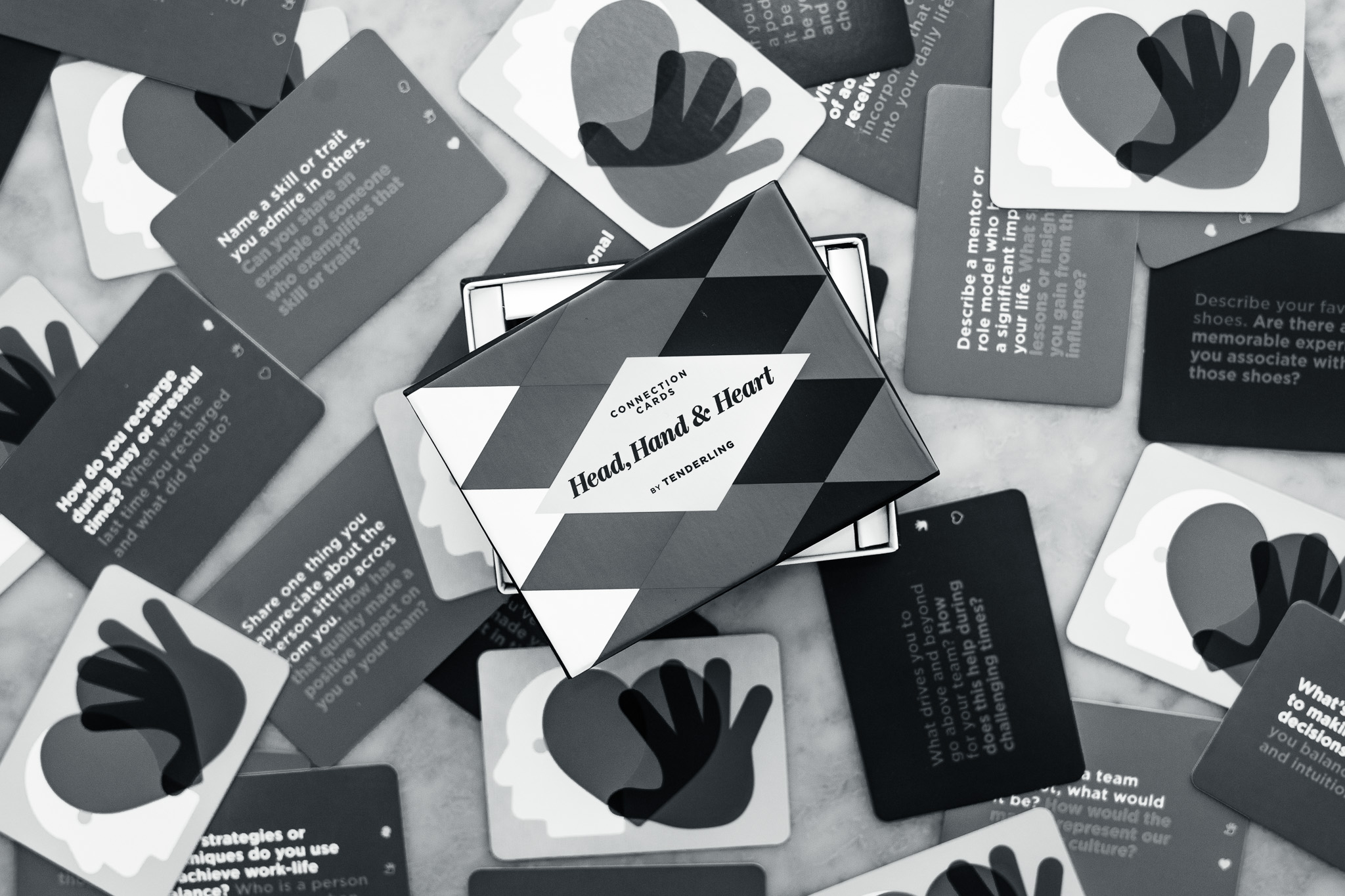 A tabletop scattered with black and white cards from a game called "Head, Hand & Heart" by The Conversation, with the game box in the center.
