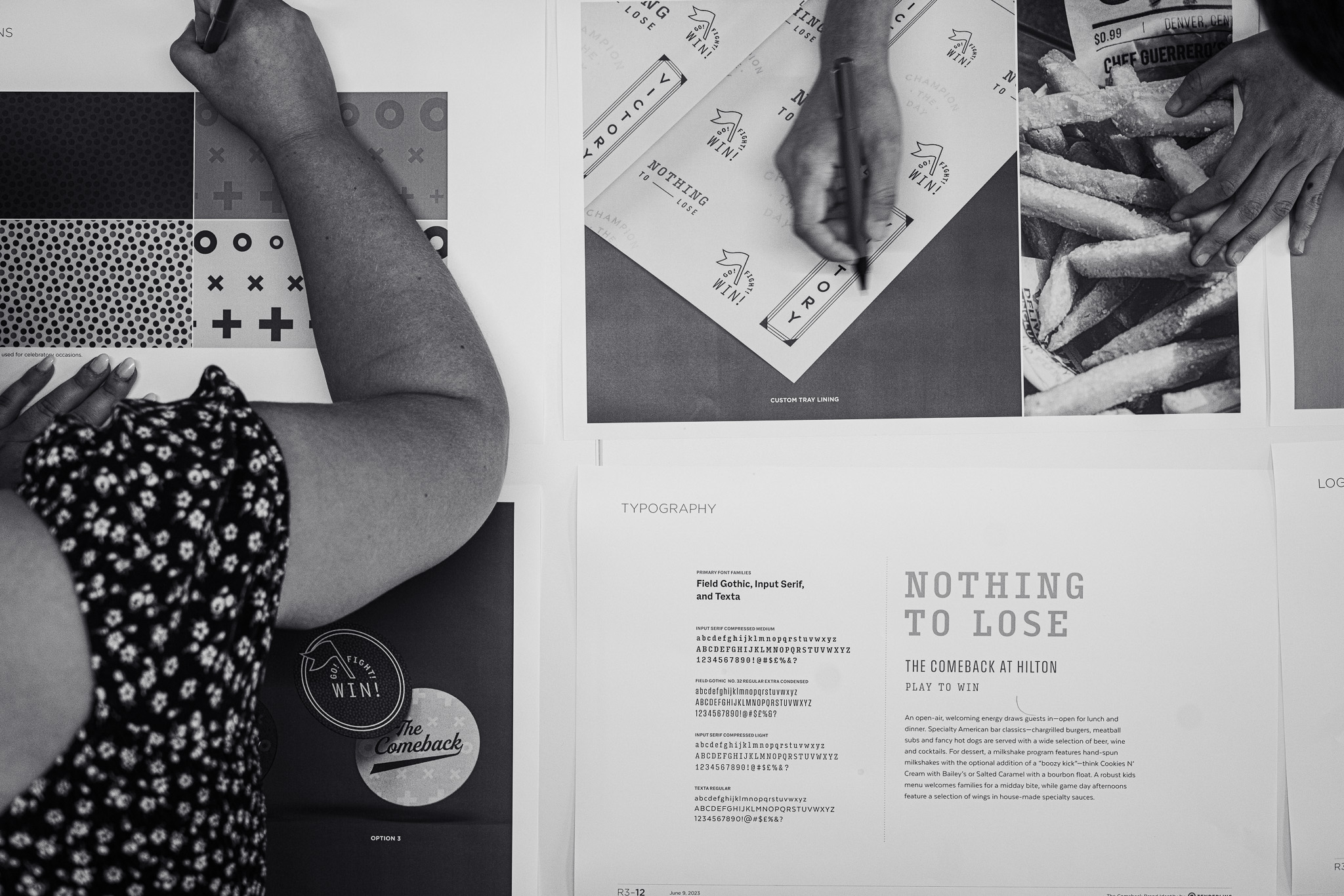 Three people work on printed design layouts, including typography samples, patterns, and food packaging mockups, using pens and markers on a table.