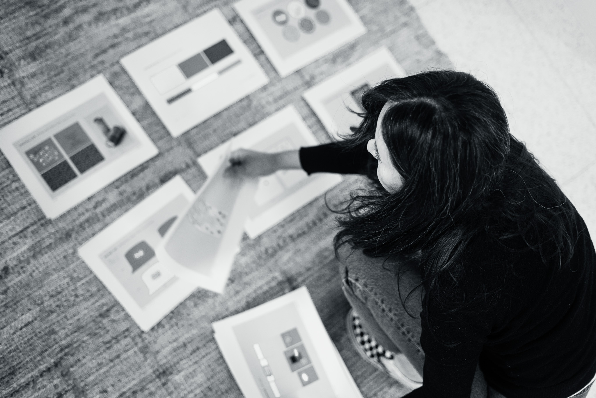 A person sits on the floor, looking at and sorting through several sheets of paper with geometric designs and diagrams printed on them.