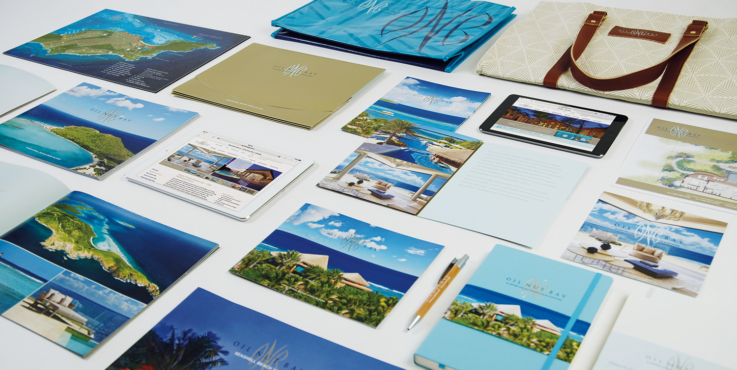 A variety of printed brochures, booklets, and digital materials featuring luxury island resort images, along with a branded tote bag, are arranged neatly on a white surface.