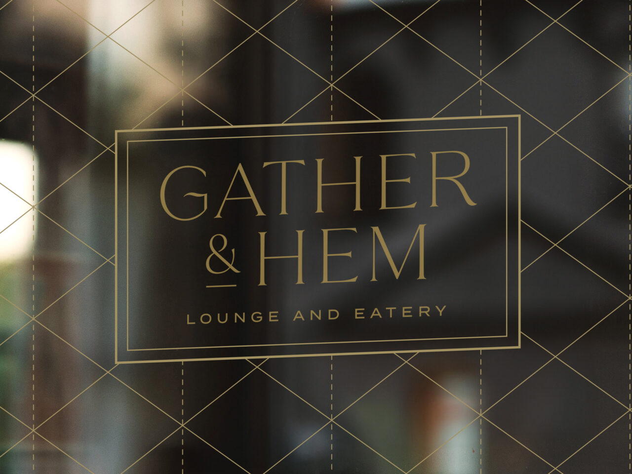 Gold text on a glass window reads “GATHER & HEM LOUNGE AND EATERY” with a grid pattern in the background.