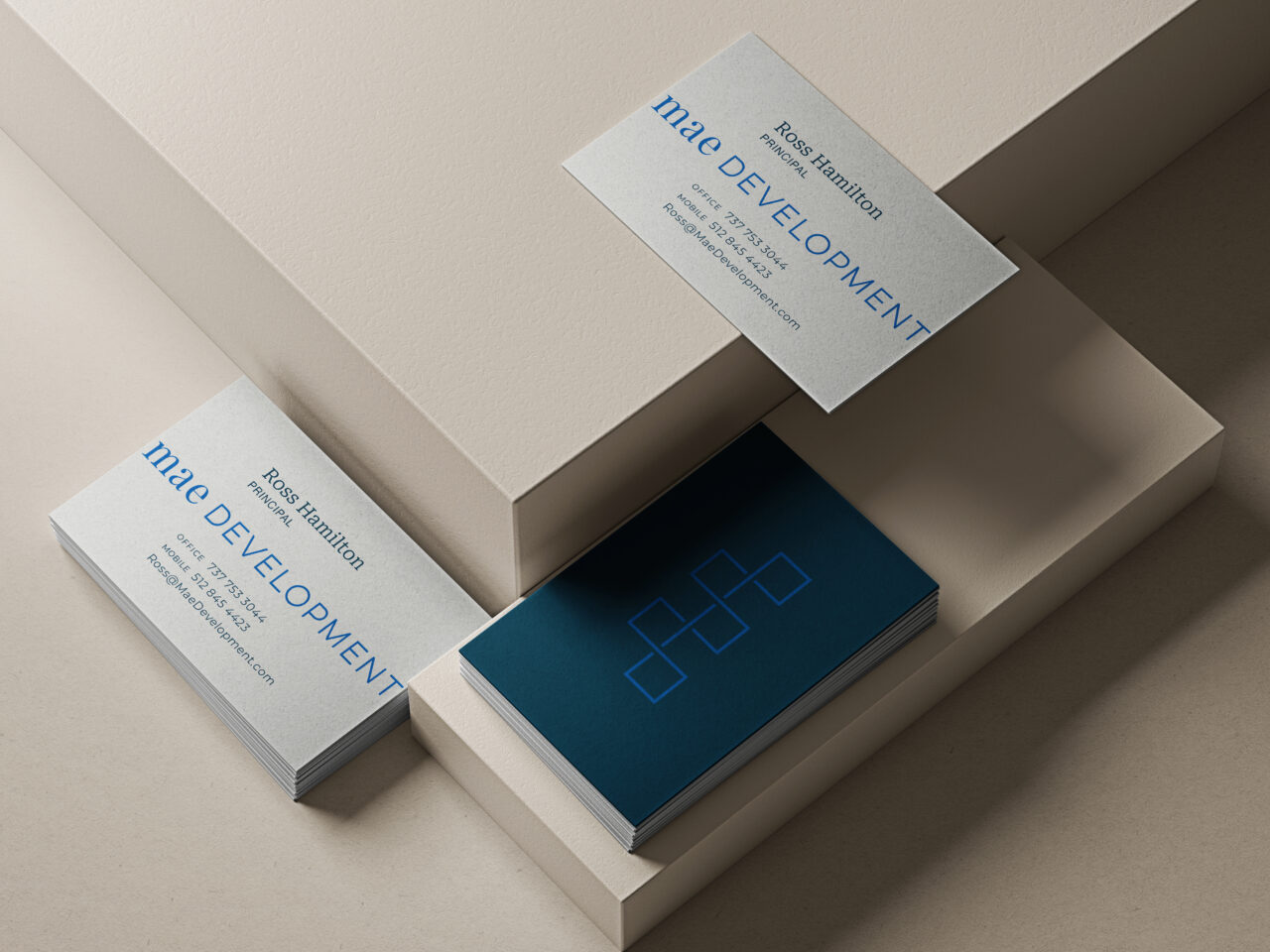 Several business cards with "milo DEVELOPMENT" and a geometric logo are arranged on beige geometric surfaces, showing both front and back designs.