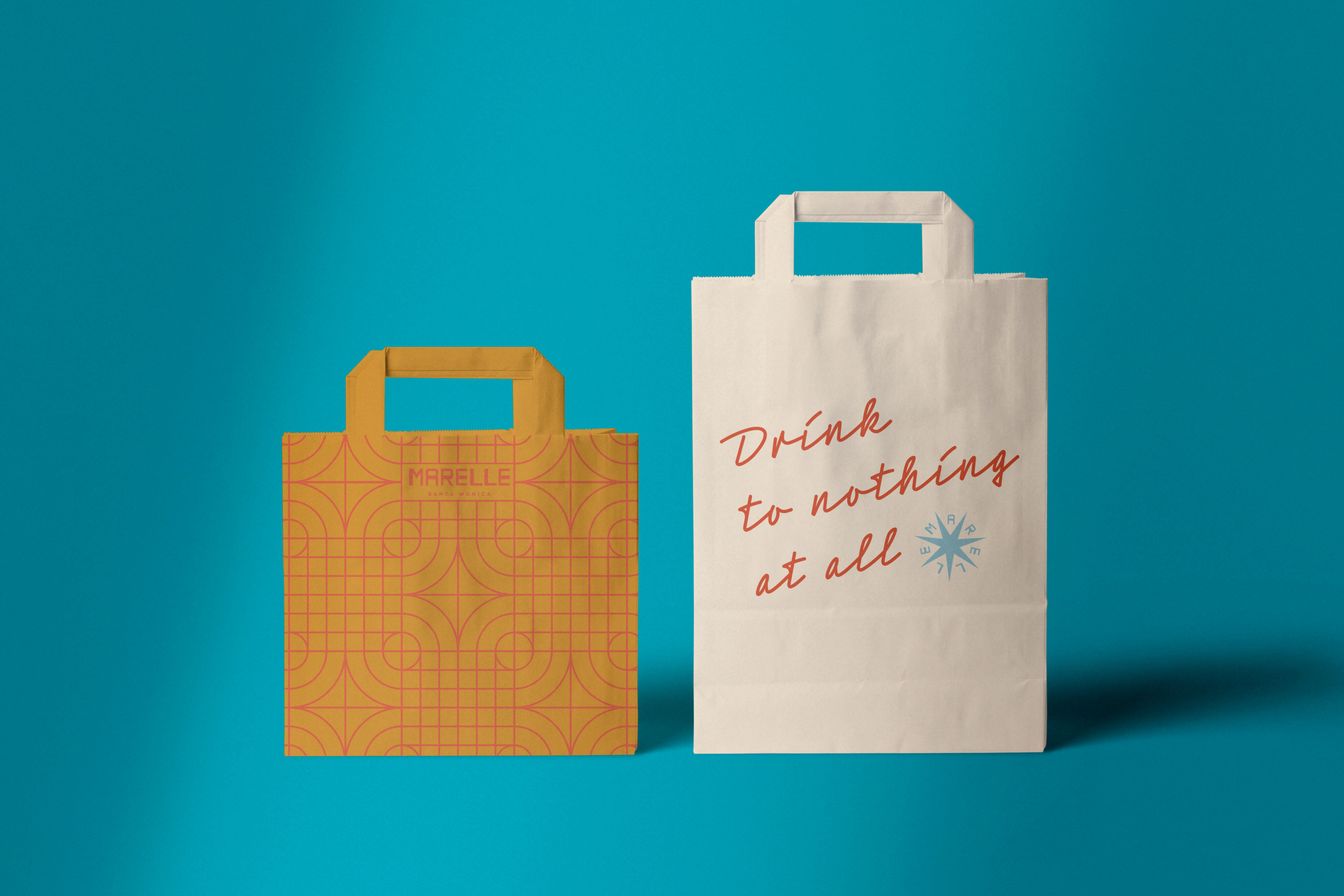 Two paper bags stand side by side against a blue background; one is yellow with a geometric pattern, the other is white with red and blue text reading "Drink to nothing at all".