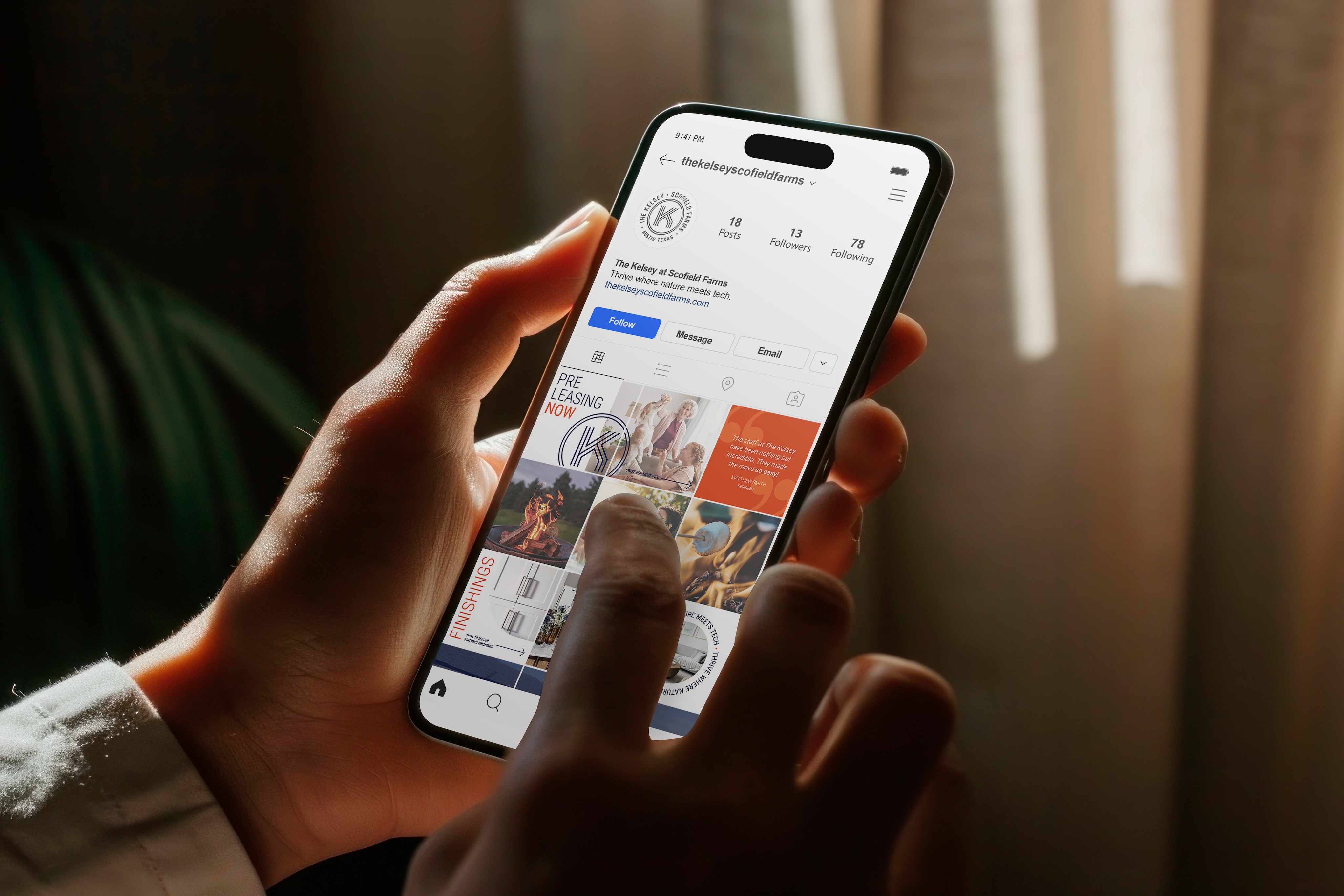 A person holds a smartphone and scrolls through an Instagram profile featuring art-themed posts, in a warmly lit indoor setting.