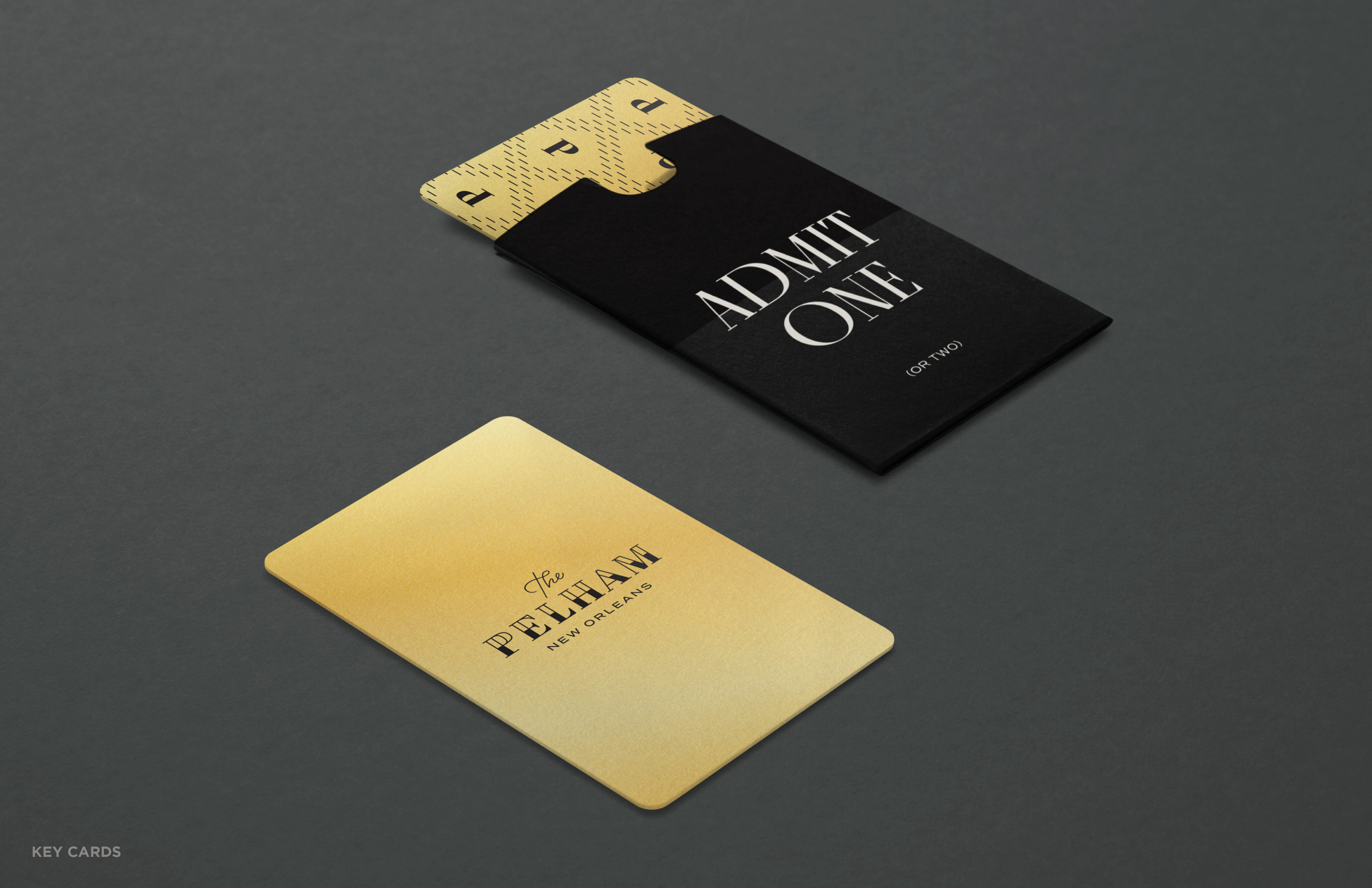 A gold card labeled “The Pelham” lies beside a black envelope marked “Admit One” containing another gold card with a geometric pattern.