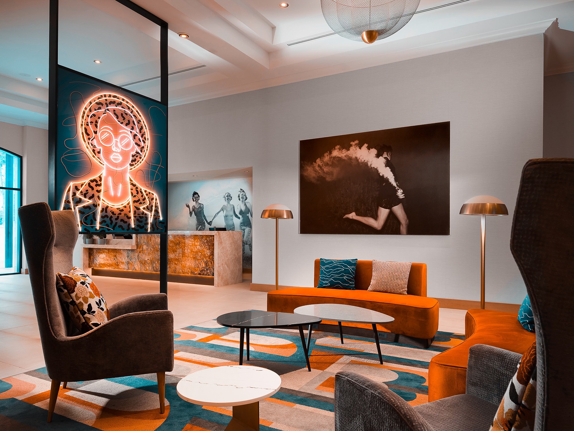 Modern hotel lobby with abstract rugs, stylish furniture, two large art pieces on the walls, and warm-toned lighting from floor lamps and ceiling fixtures.