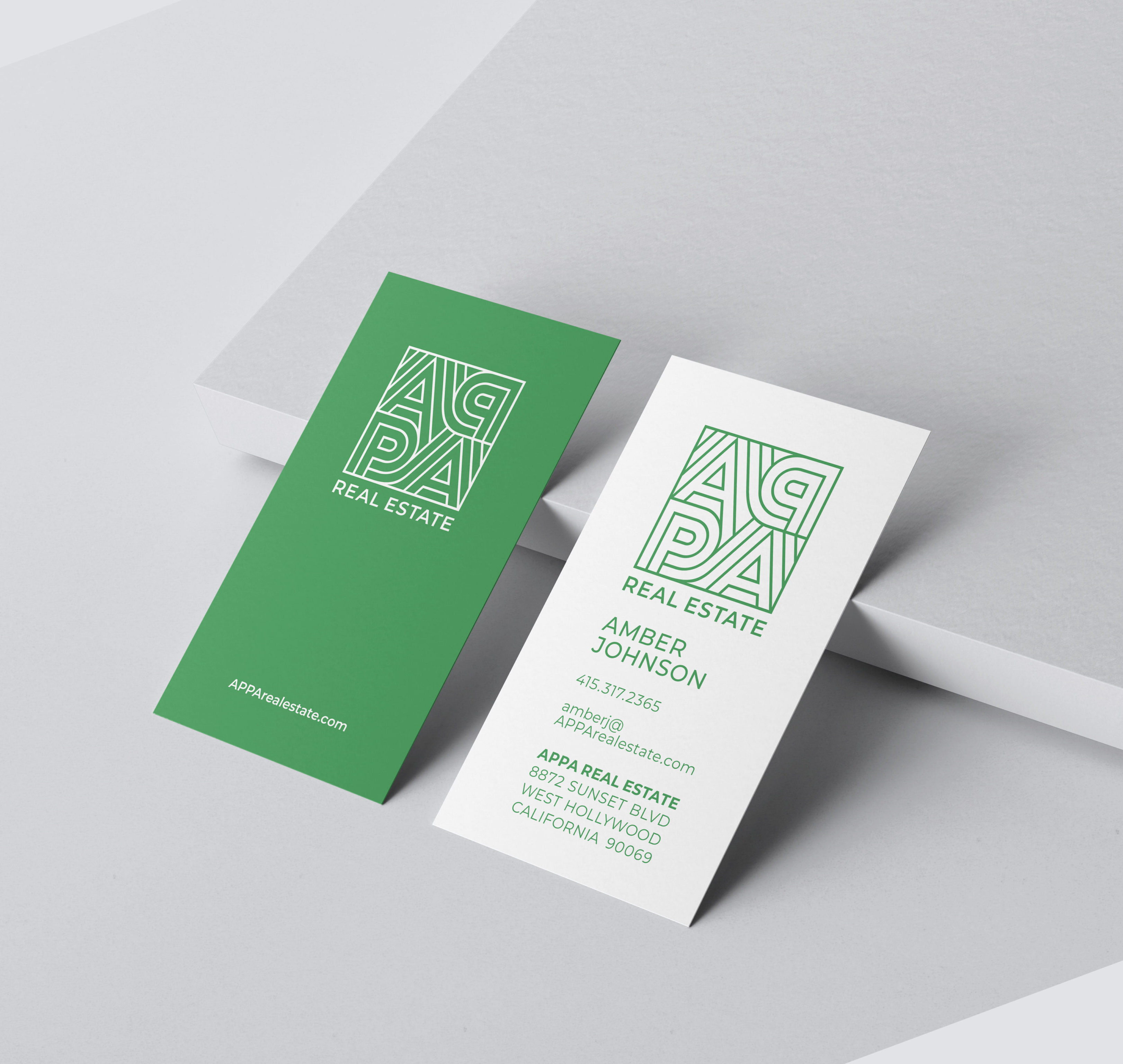 Two APPA Real Estate business cards, one green and one white, showing company logo, contact details for Amber Johnson, and the business address on a light grey background.