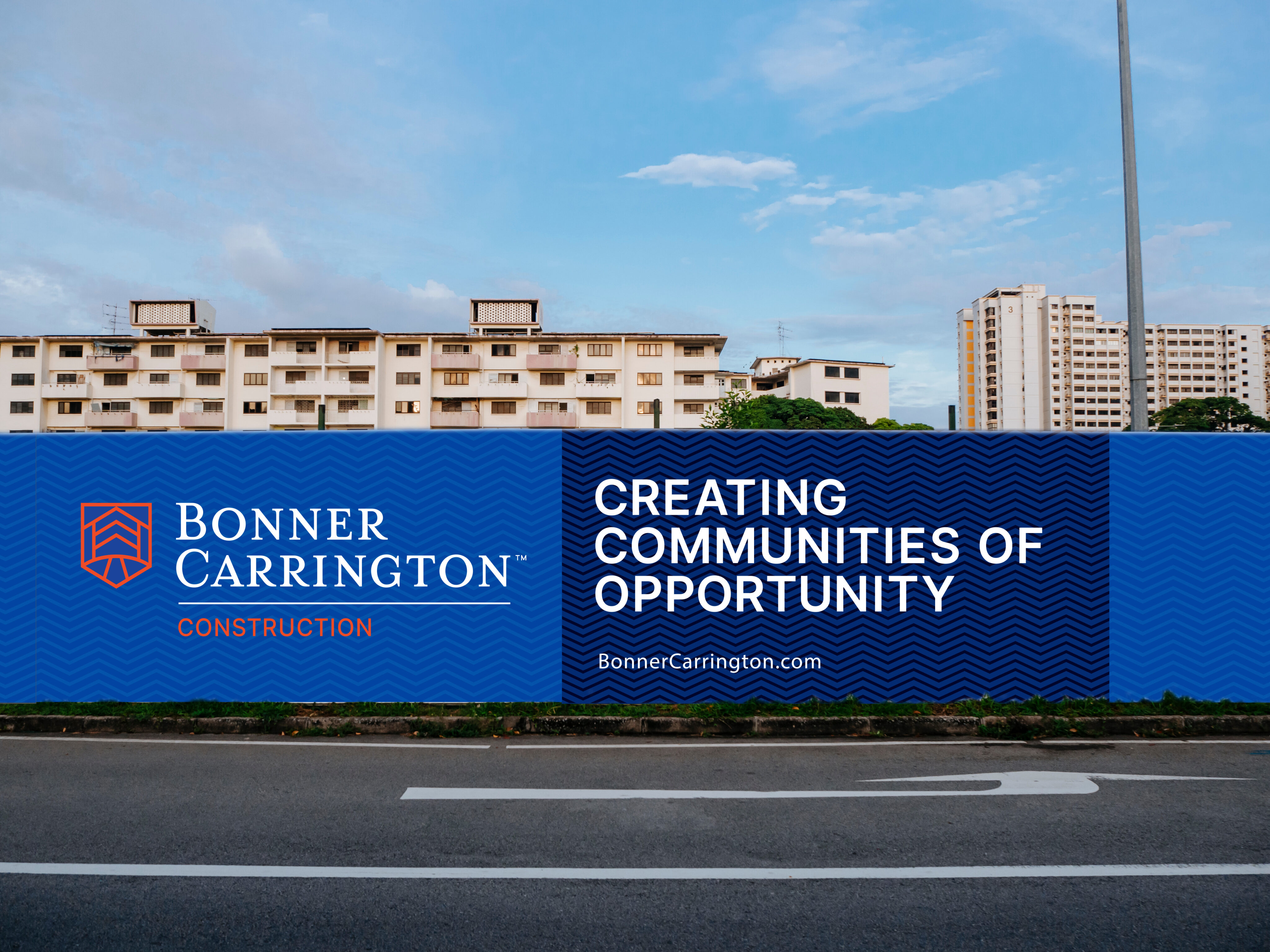 A blue construction site barrier displays the Bonner Carrington logo and the slogan "Creating Communities of Opportunity" in front of residential buildings.