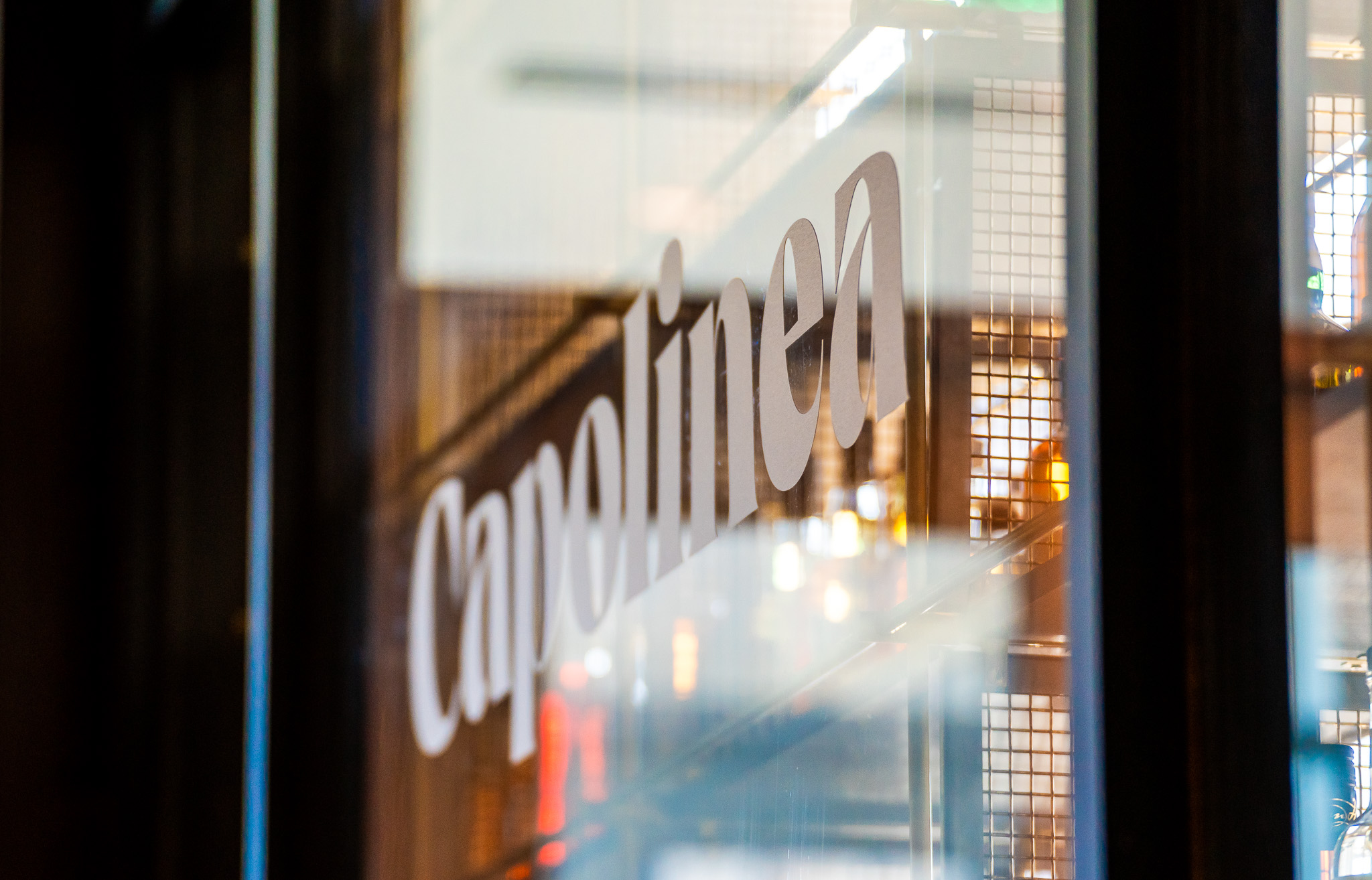 The word "capolinea" is printed on a glass panel, with a blurred, industrial-style interior visible through the glass.