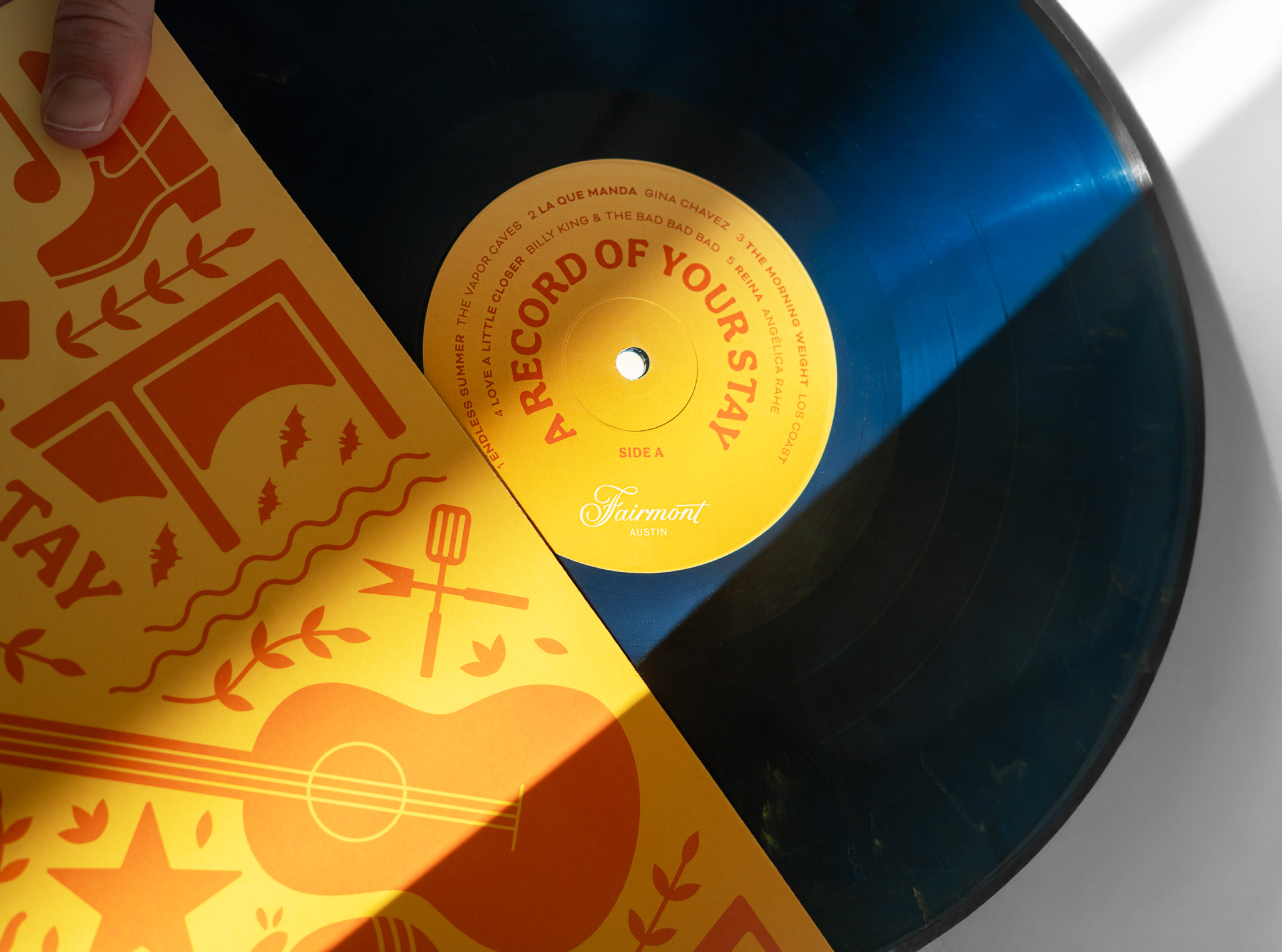 A close-up of a vinyl record labeled "A Record of Your Stay" by Fairmont Austin, partially pulled from a yellow illustrated sleeve with musical and travel-themed graphics.