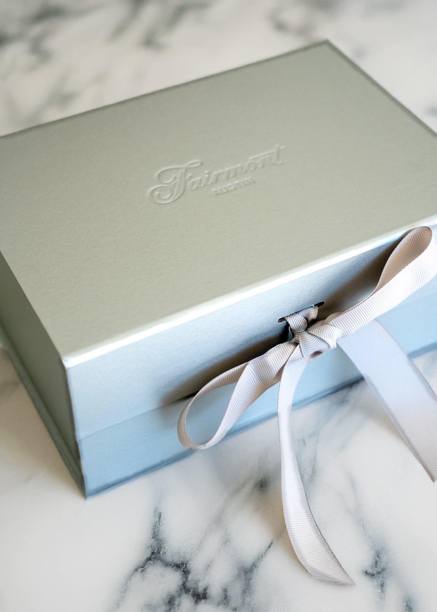A light blue Fairmont box with a white ribbon bow sits on a white marble surface.