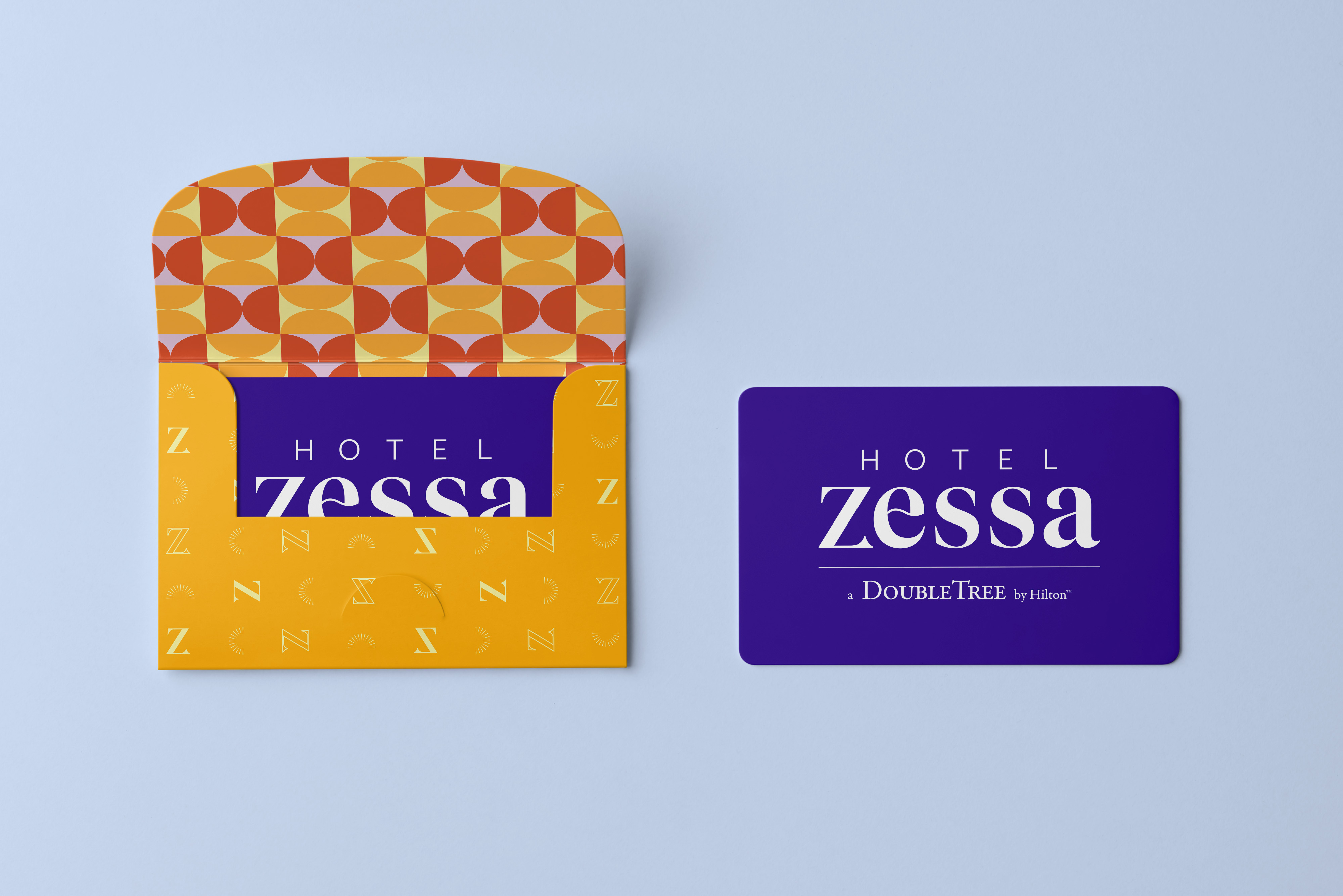 A purple hotel key card labeled "Hotel Zessa" and "DoubleTree by Hilton" next to a patterned yellow and orange key card holder on a light blue background.