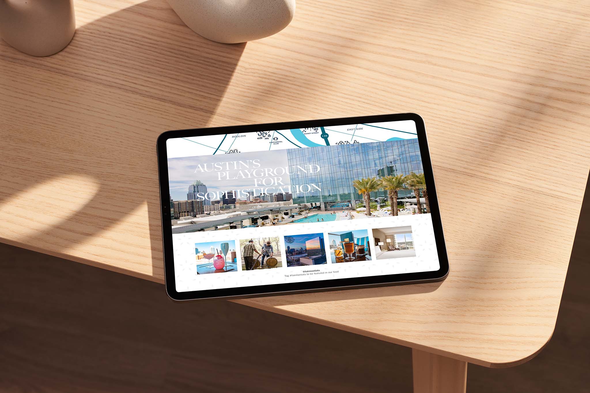A tablet on a wooden table displays a website featuring a modern glass building, palm trees, and the text “Austin’s Playground for Sophistication.”.