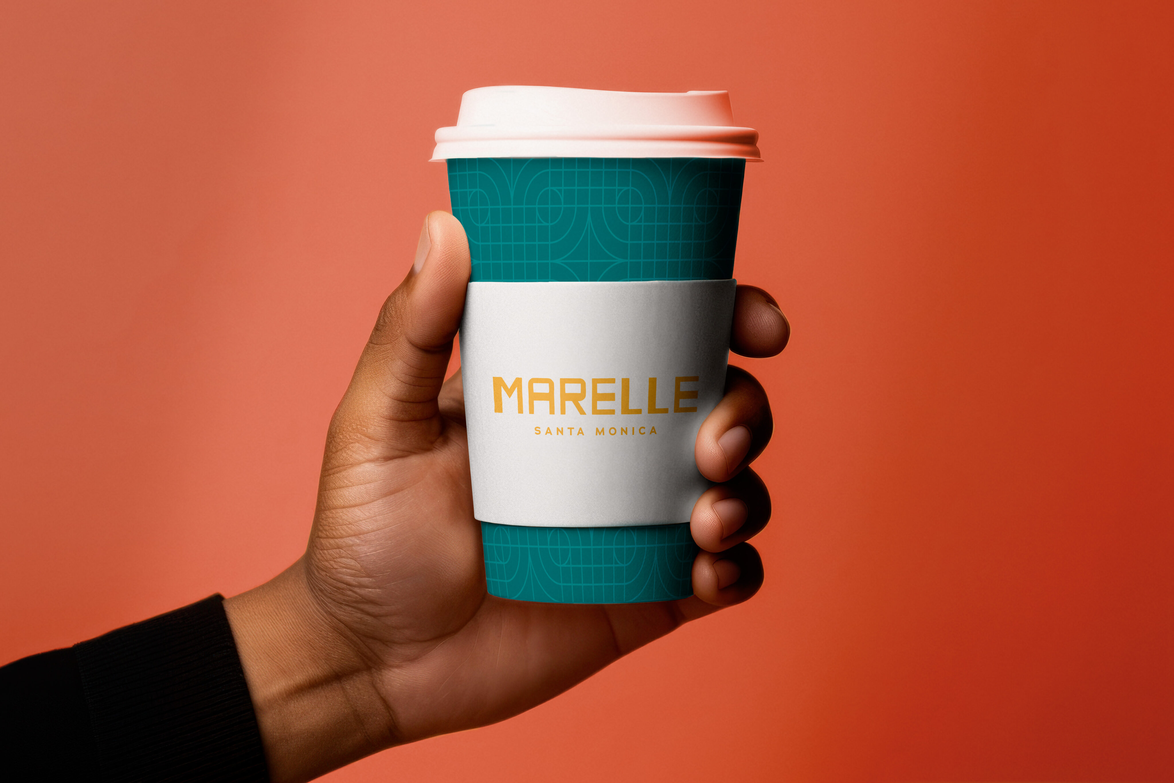 A hand holds a teal coffee cup with a white sleeve labeled "MARELLE SANTA MONICA" against an orange background.