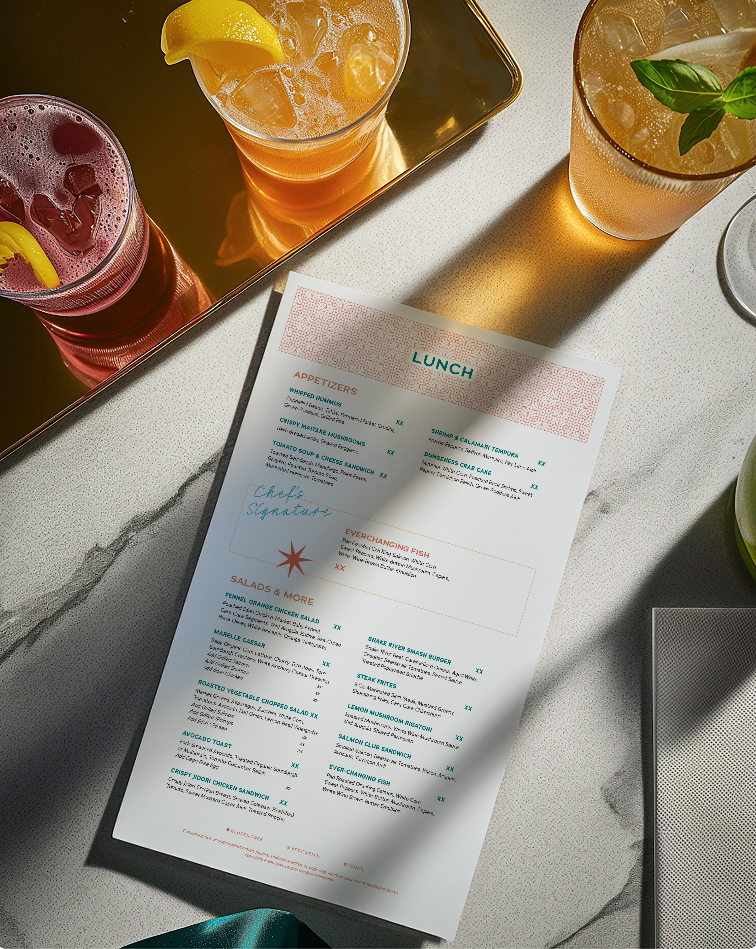 A lunch menu on a marble table with three colorful drinks, one garnished with lemon, displayed alongside a gold tray.