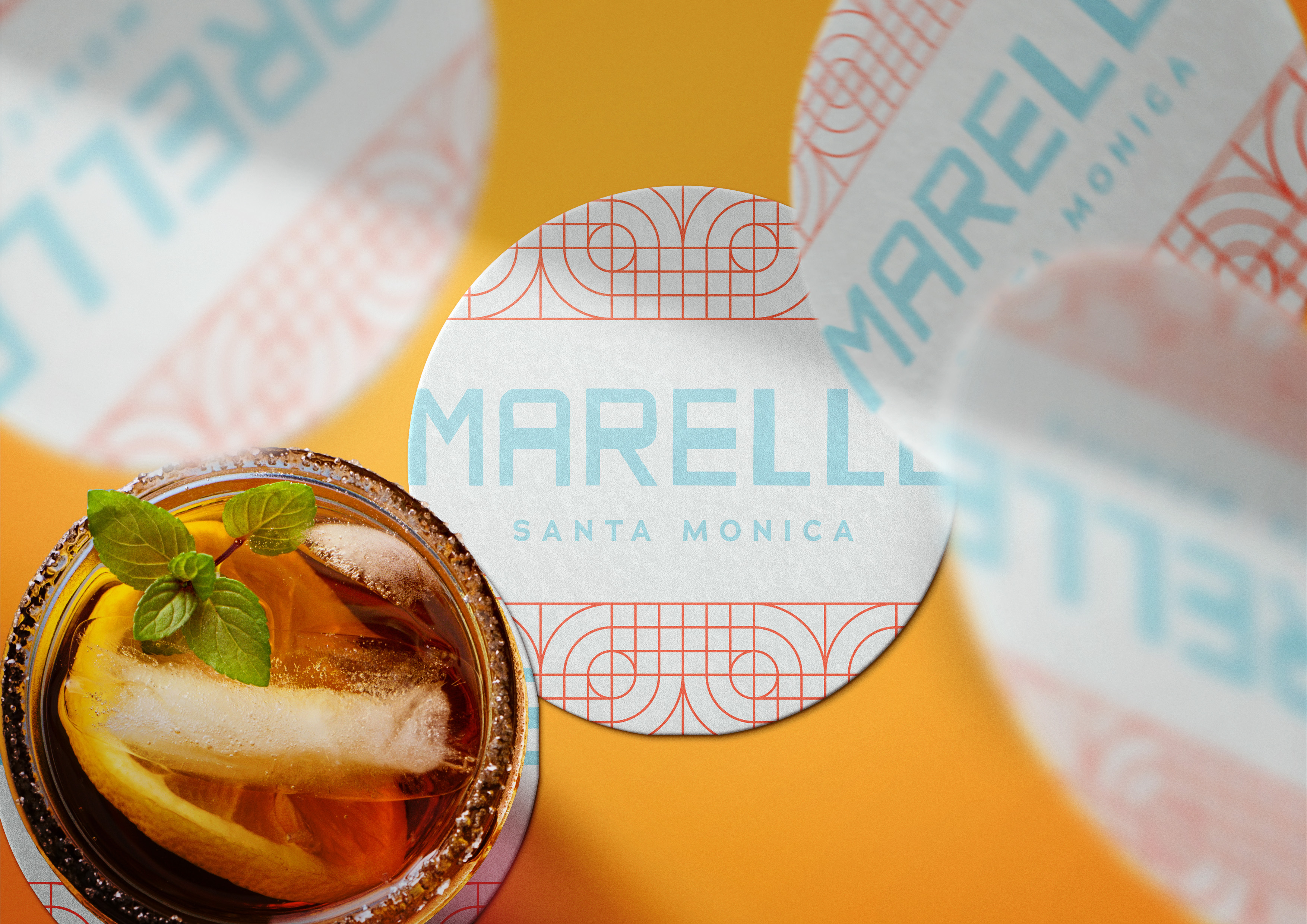 A close-up of a drink with ice, lemon, and mint next to a round coaster that reads "MARELLE SANTA MONICA" on an orange surface.