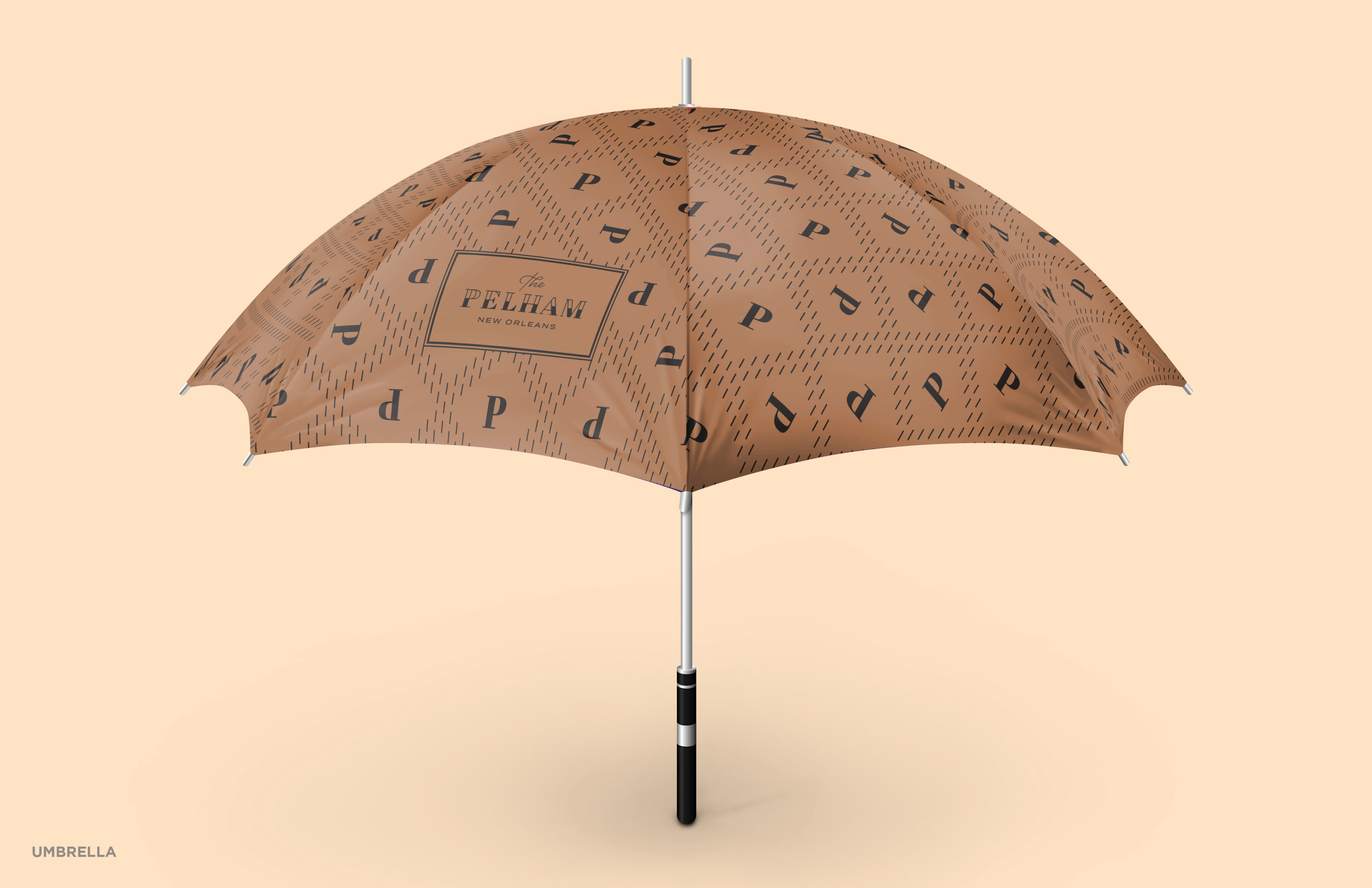 A light brown umbrella with a repeating black pattern and "The Pelham New Orleans" logo printed on it, standing open on a neutral background.