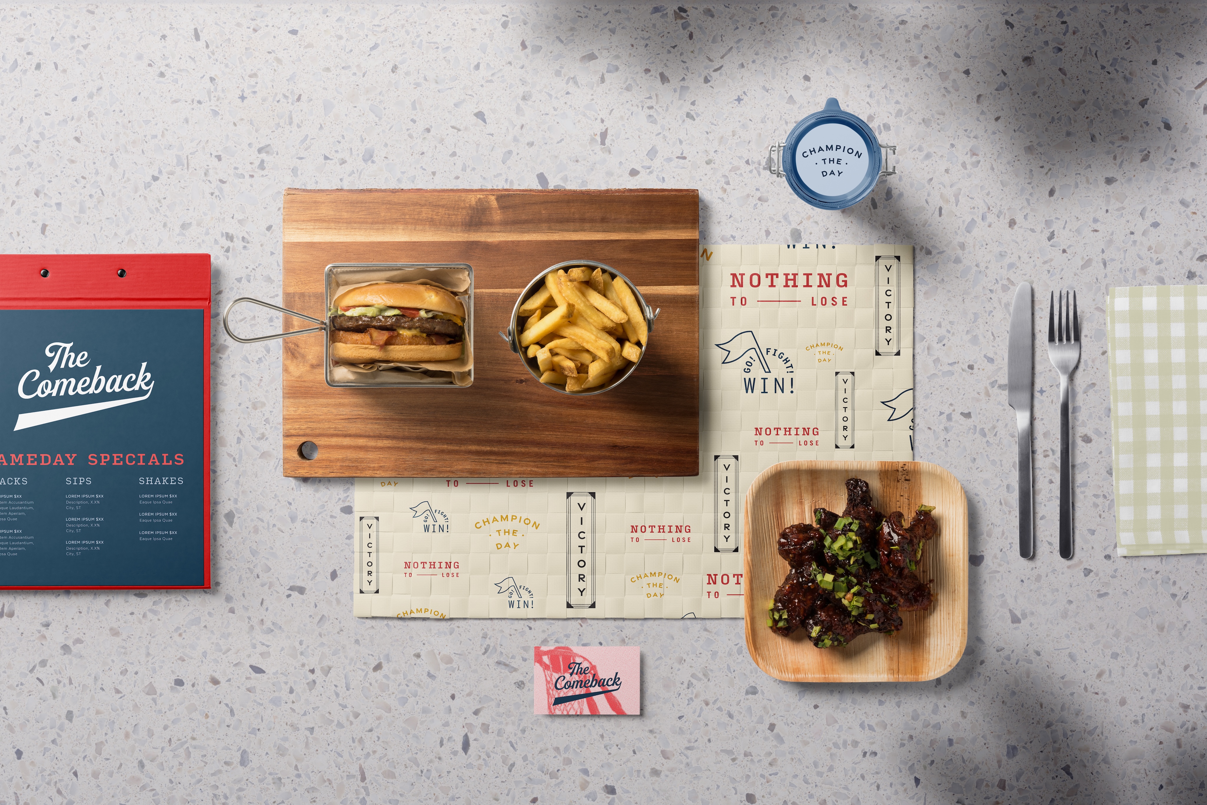 A cheeseburger with fries on a wooden board, a plate of glazed chicken wings, utensils, a drink cup, a menu, and napkins arranged on a speckled tabletop.
