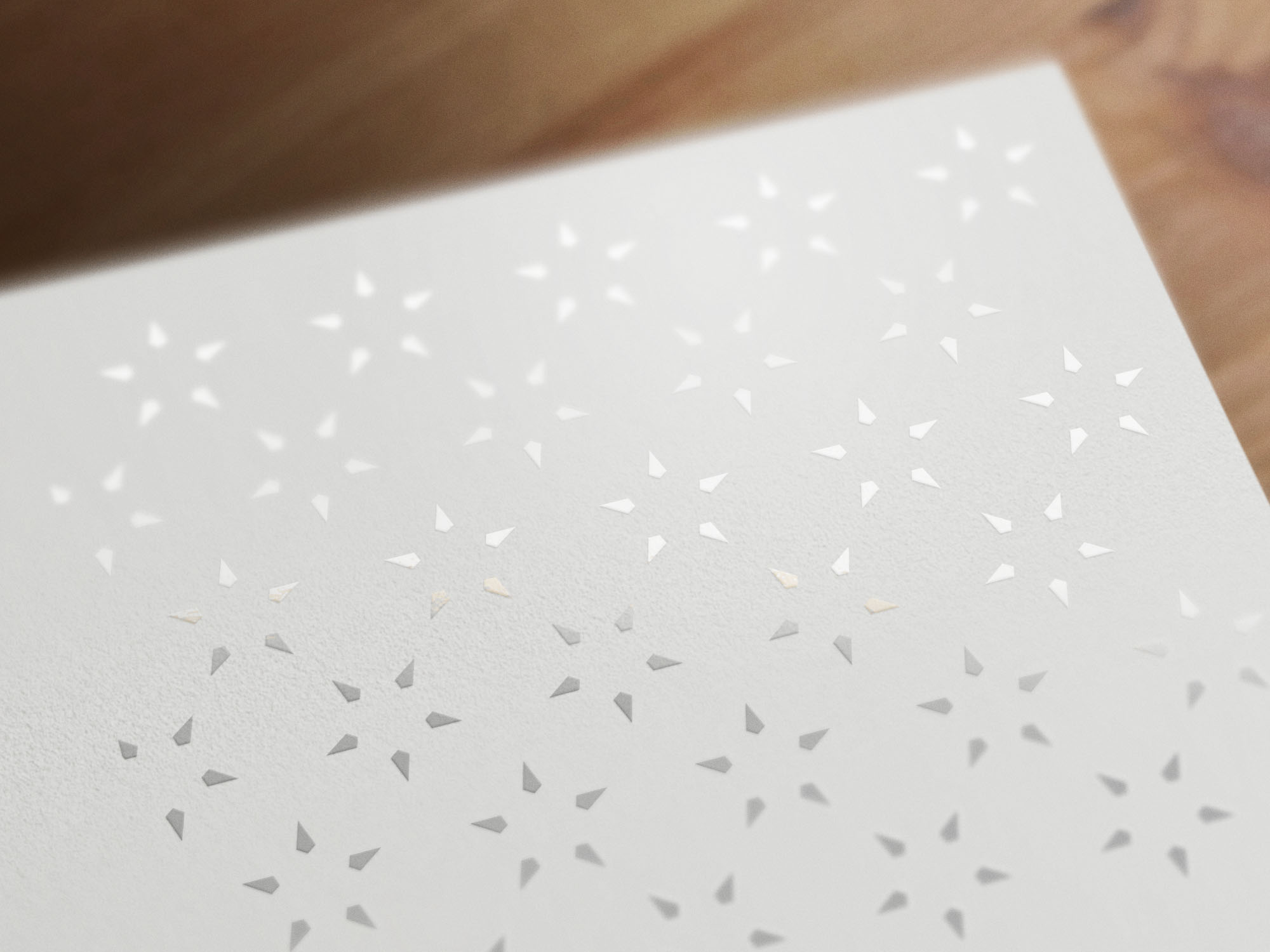 Close-up of a white textured sheet with a pattern of small, evenly spaced, triangular cutouts, placed on a wooden surface.