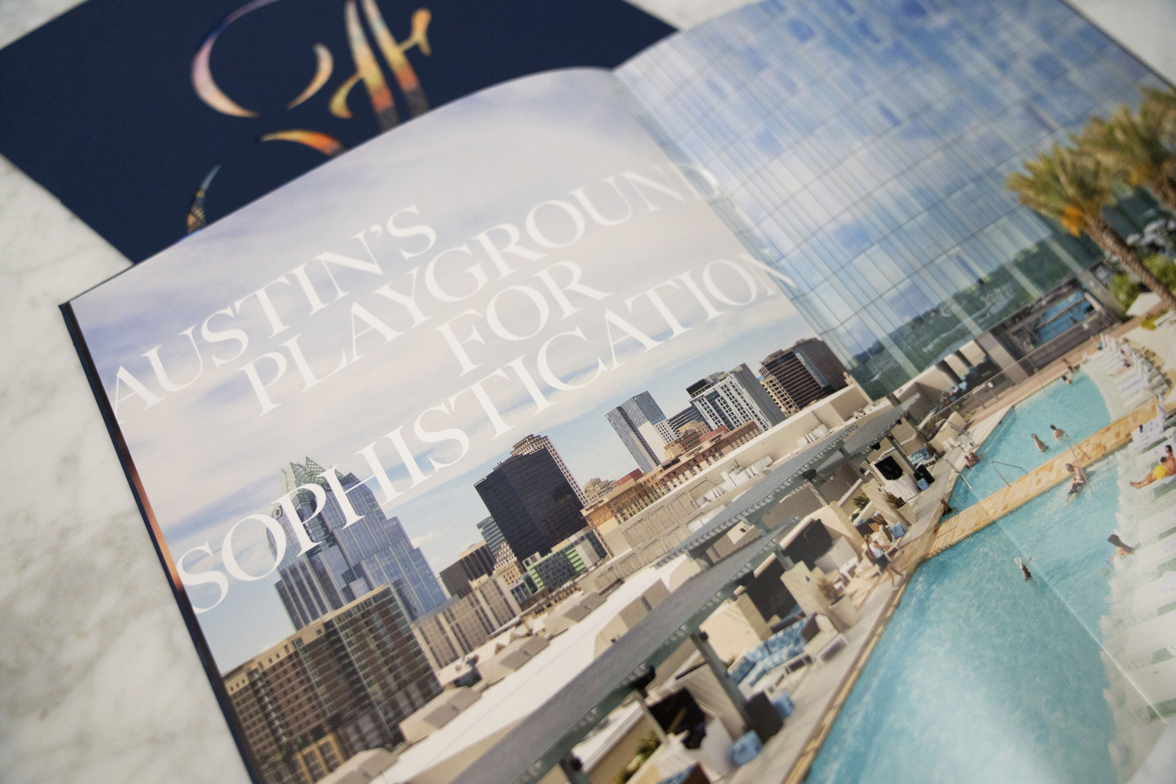 An open magazine shows a city skyline and rooftop pool with the text "Austin's Playground for Sophistication" across the image.