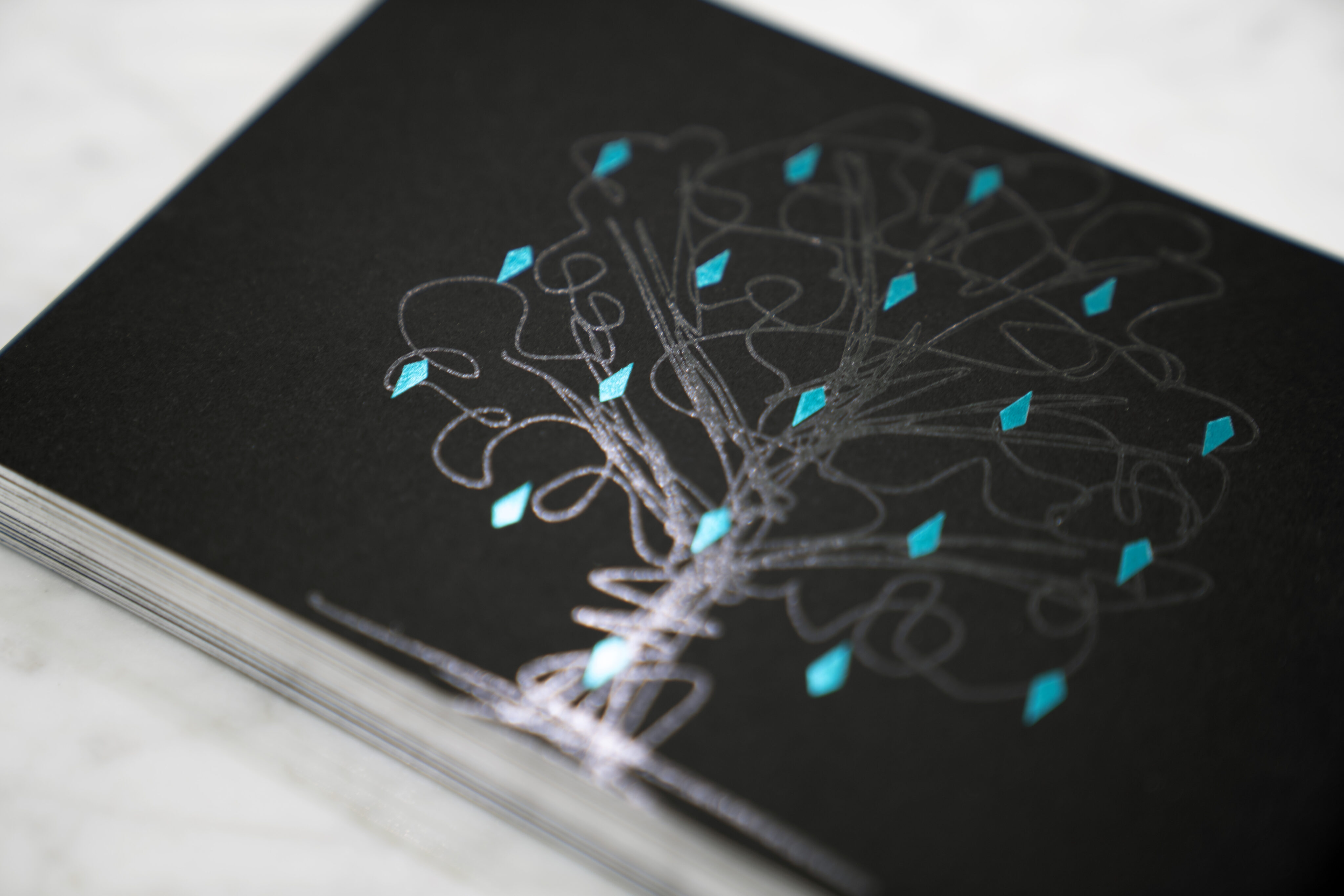 A close-up of a black card featuring a silver tree design with blue geometric leaf accents.