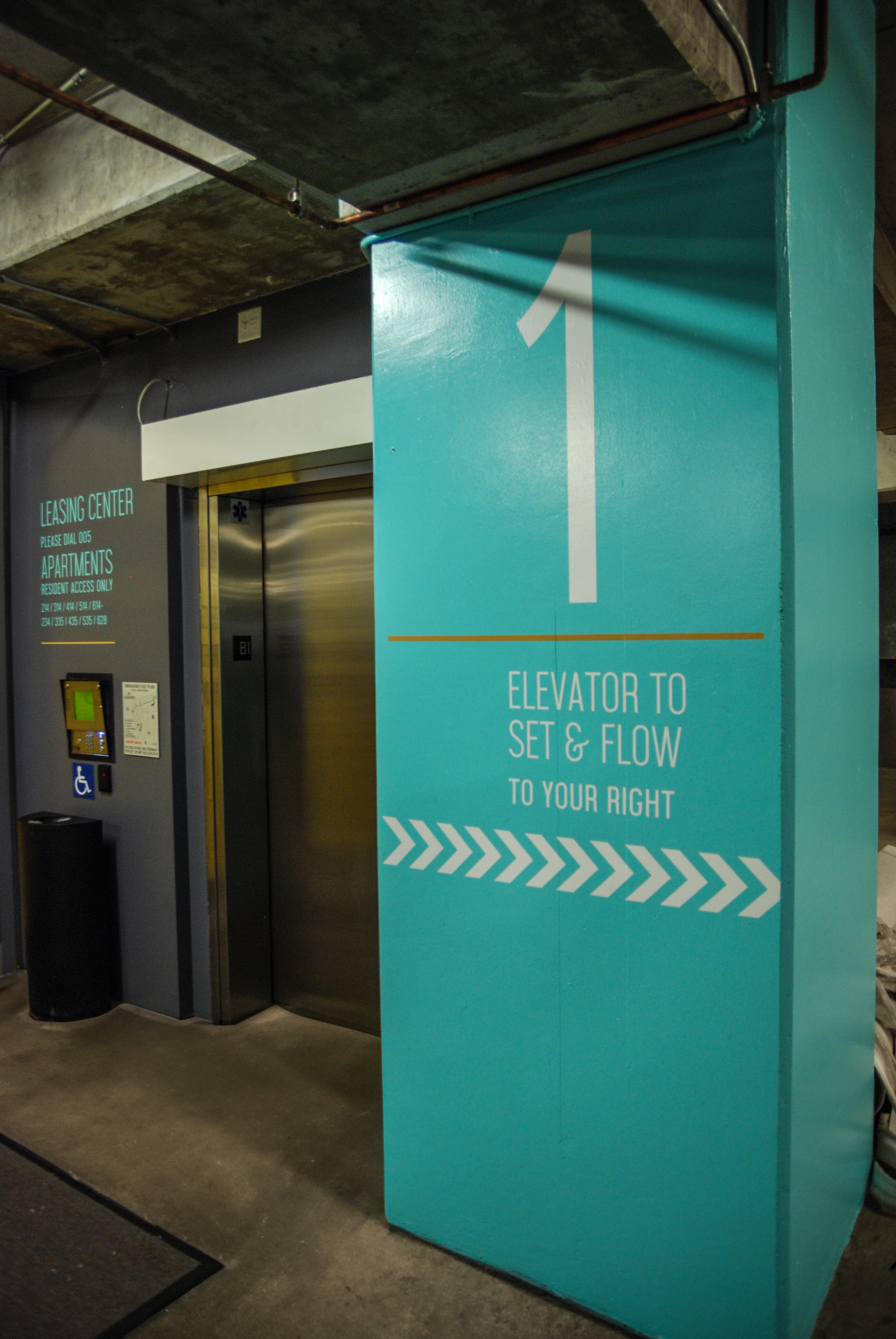 Elevator area on parking level 1 with signs for leasing center and directions to elevator; teal and gray color scheme.
