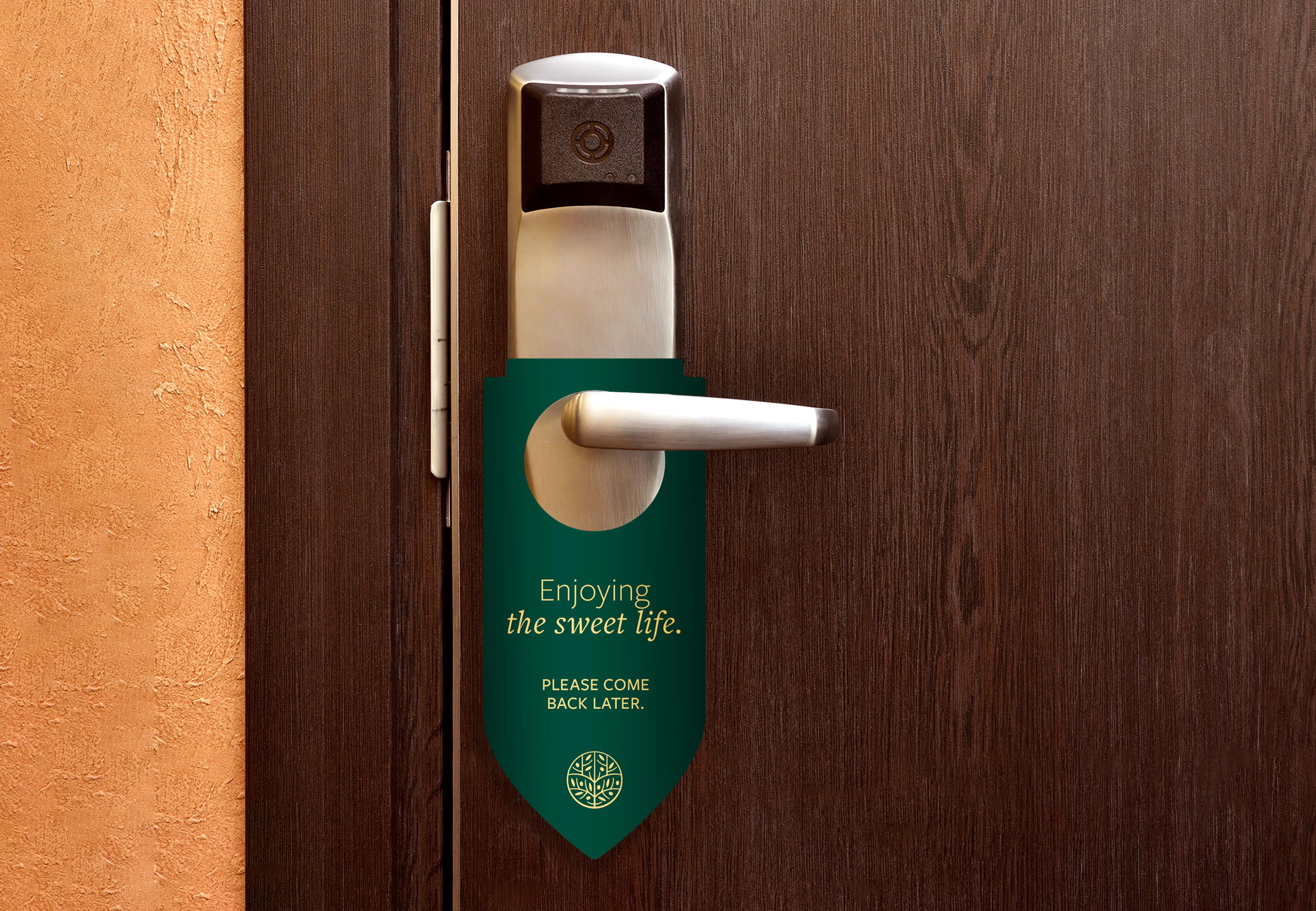 A dark green door hanger on a hotel room door handle reads, "Enjoying the sweet life. Please come back later.