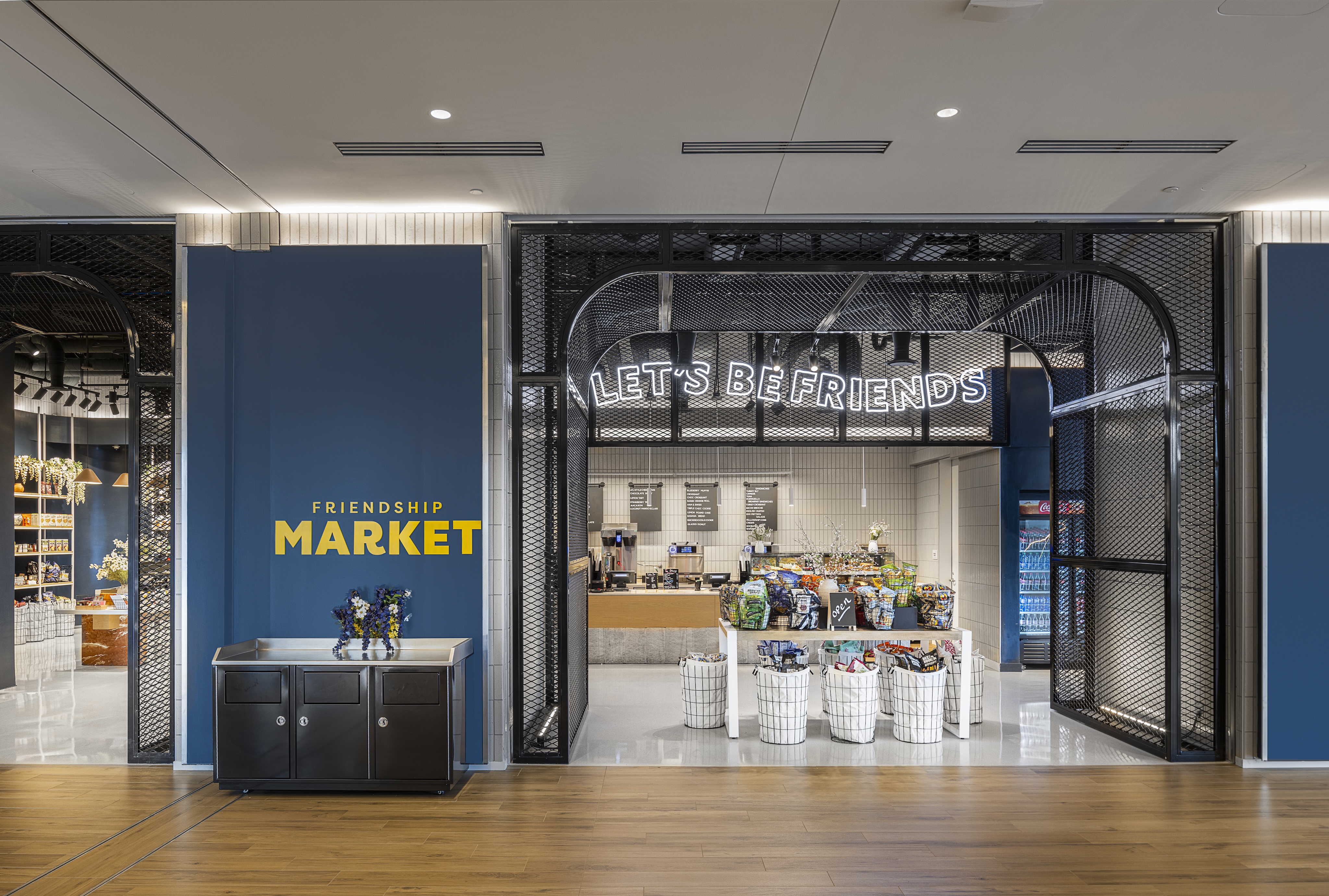 Retail store entrance with "LET'S BE FRIENDS" sign above, display of products inside, blue walls, and "FRIENDSHIP MARKET" text on the left.