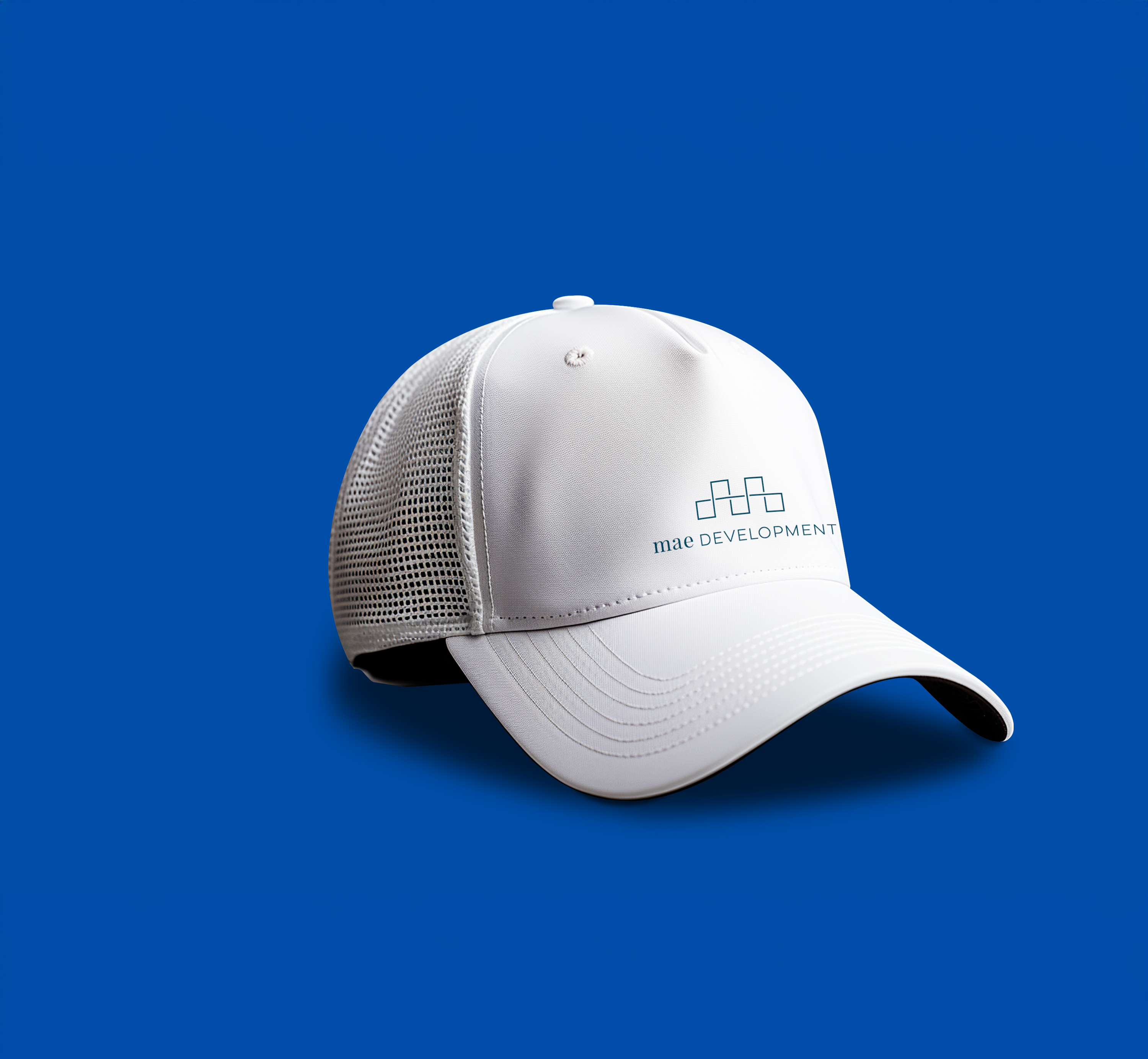 A white mesh back baseball cap with "mae DEVELOPMENT" and a geometric logo printed on the front, displayed on a solid blue background.