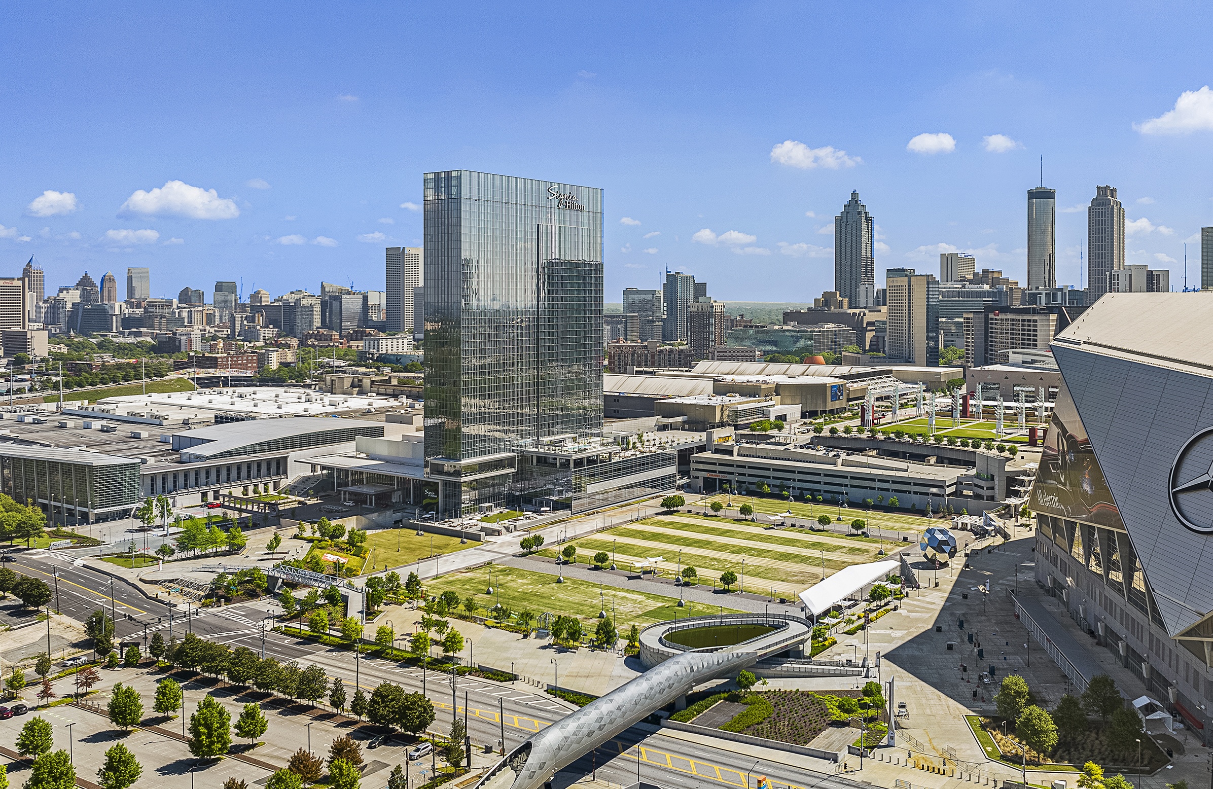 Aerial view of downtown Atlanta featuring tall glass skyscrapers, green spaces, and city streets under a clear blue sky.