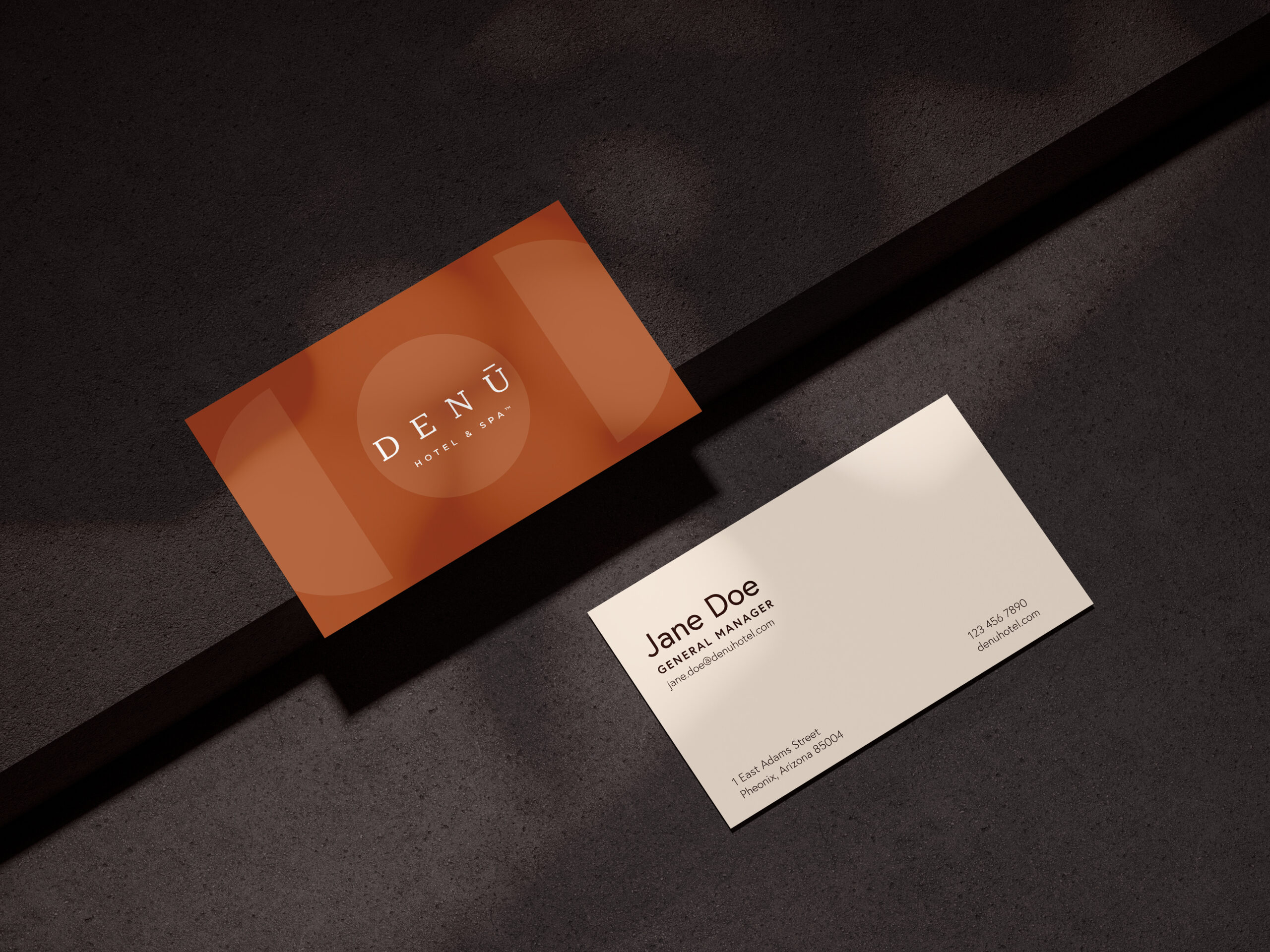 Two business cards on a dark surface; one shows the DENÜ Hotel & Spa logo, the other displays contact details for Jane Doe, General Manager.