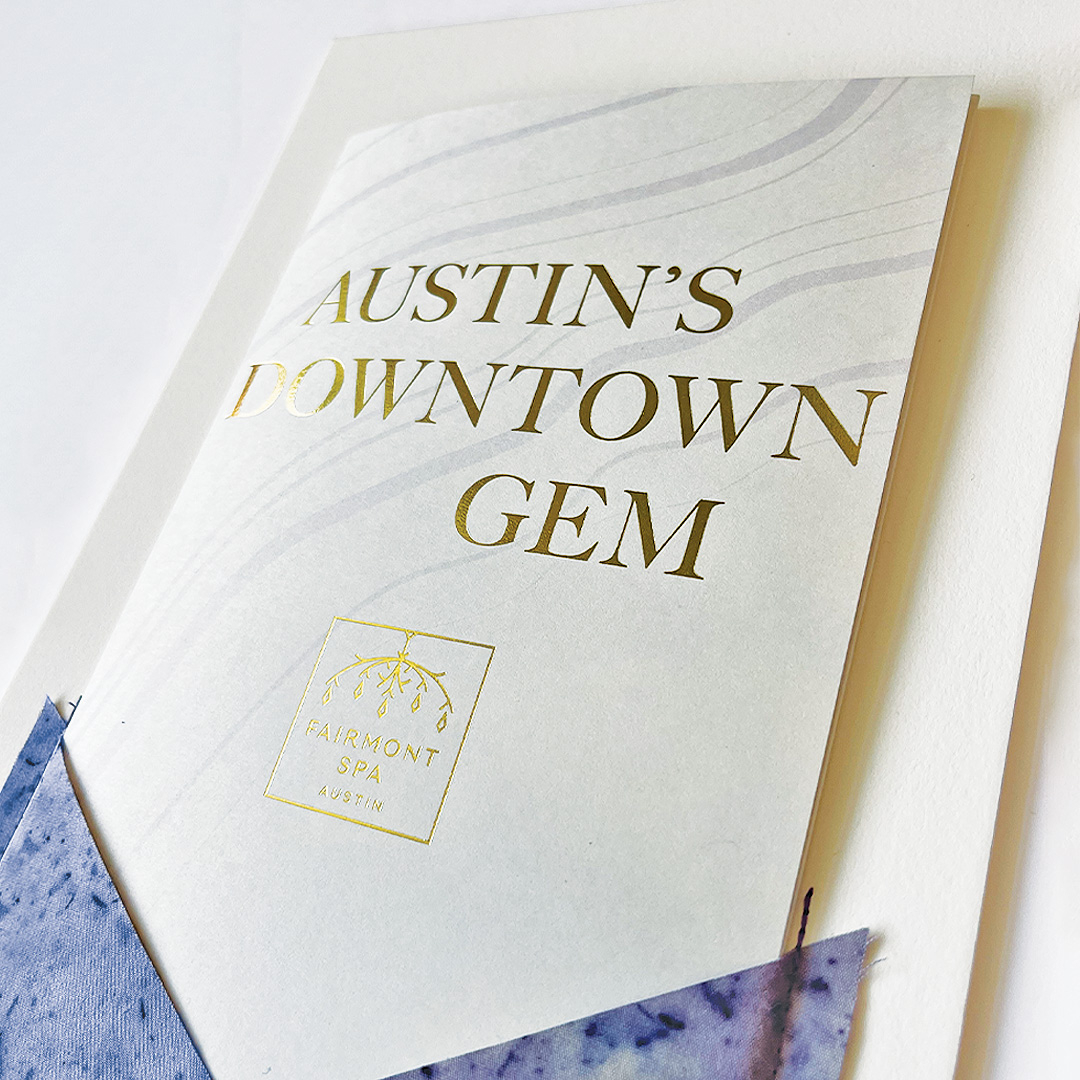 A brochure with the title "Austin's Downtown Gem" and a gold Fairmont Spa Austin logo, partially tucked into a purple holder.