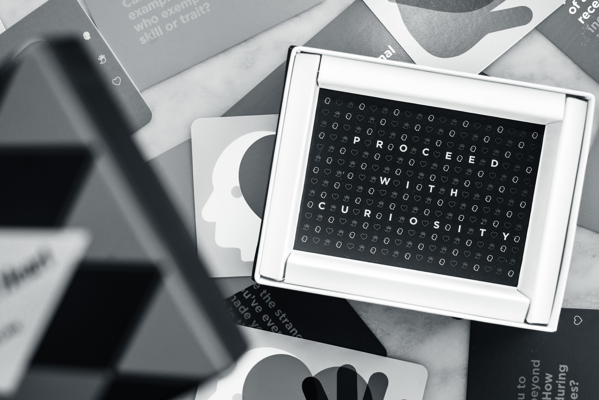 A monochrome photo of a card box displaying the words "PROCEED WITH CURIOSITY," surrounded by various other cards with abstract designs and text.