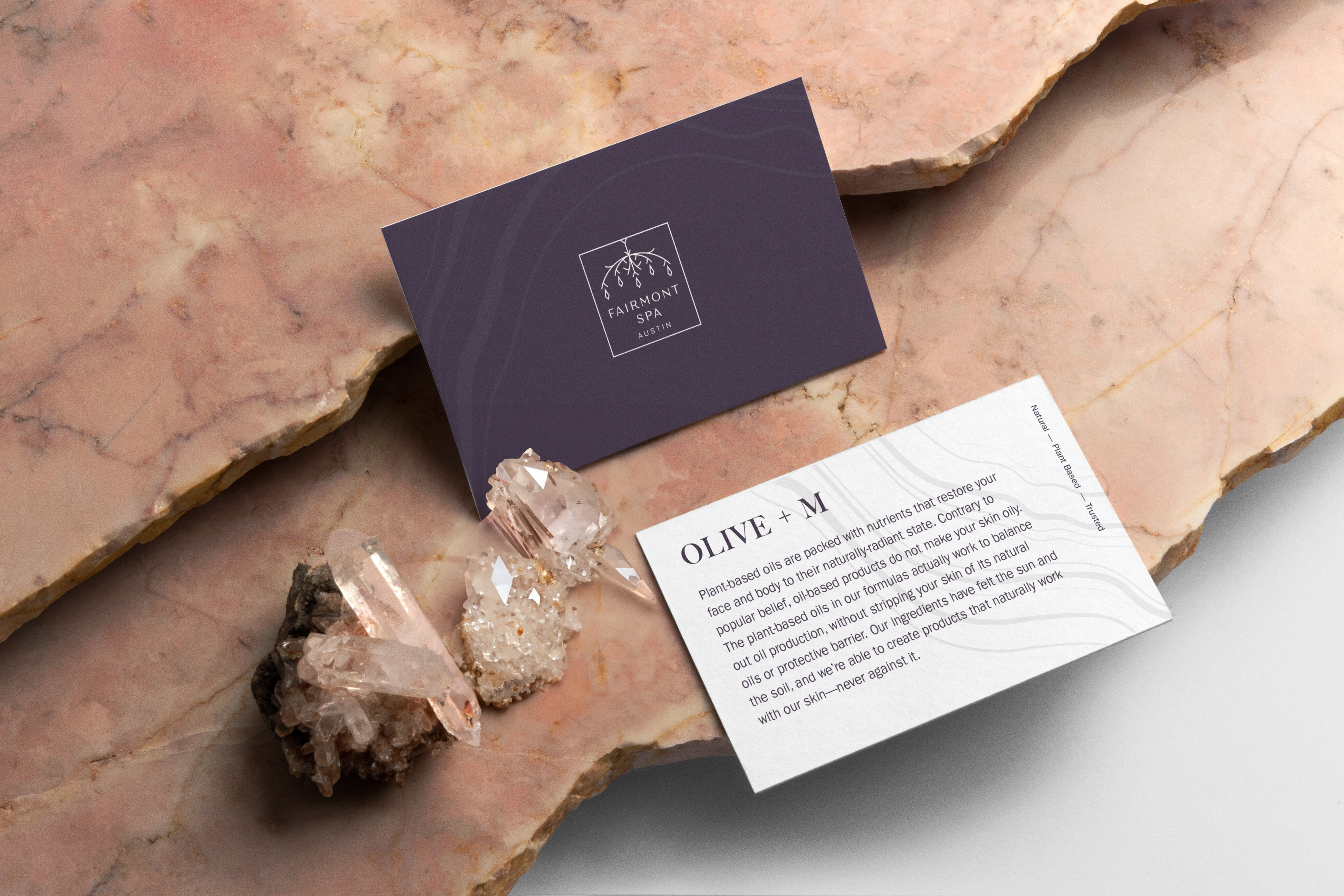 Two business cards, one navy and one white, rest on pink marble beside clear quartz crystals. The cards showcase branding and highlight brand strategy and design solutions with elegant informational text.