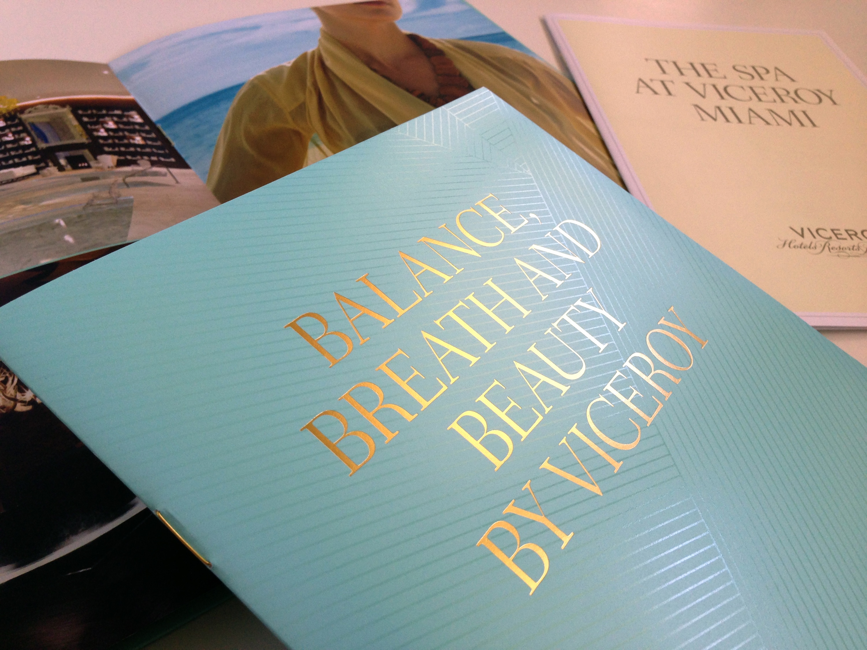 A close-up of brochures, with the front one titled "Balance Breath and Beauty by Viceroy" in gold text, showcases brand strategy and design solutions alongside images and "The Spa at Viceroy Miami.