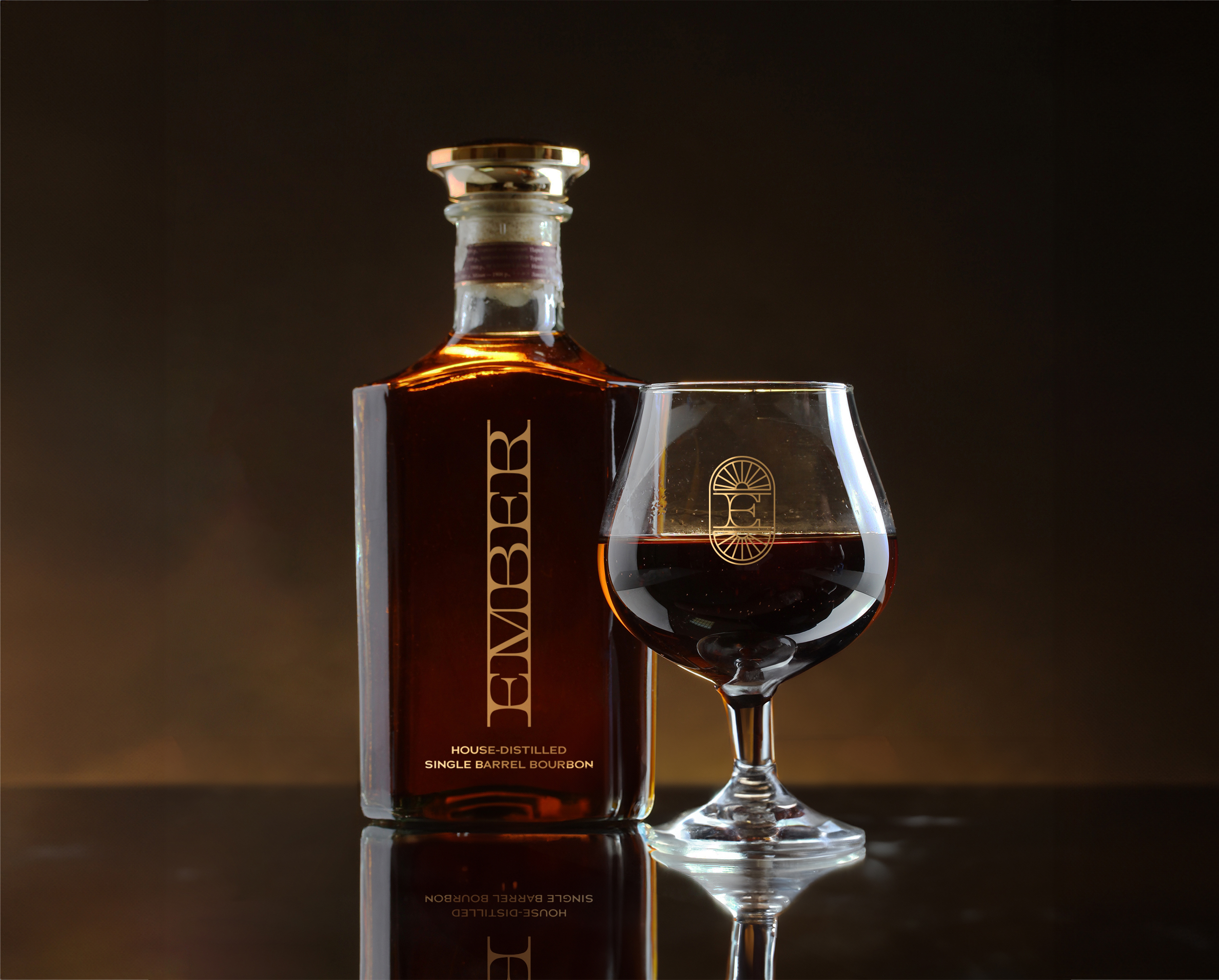 A bottle of dark liquor labeled "EMBER" stands next to a filled glass, both featuring gold accents, against a dark background—showcasing refined brand strategy and design solutions.