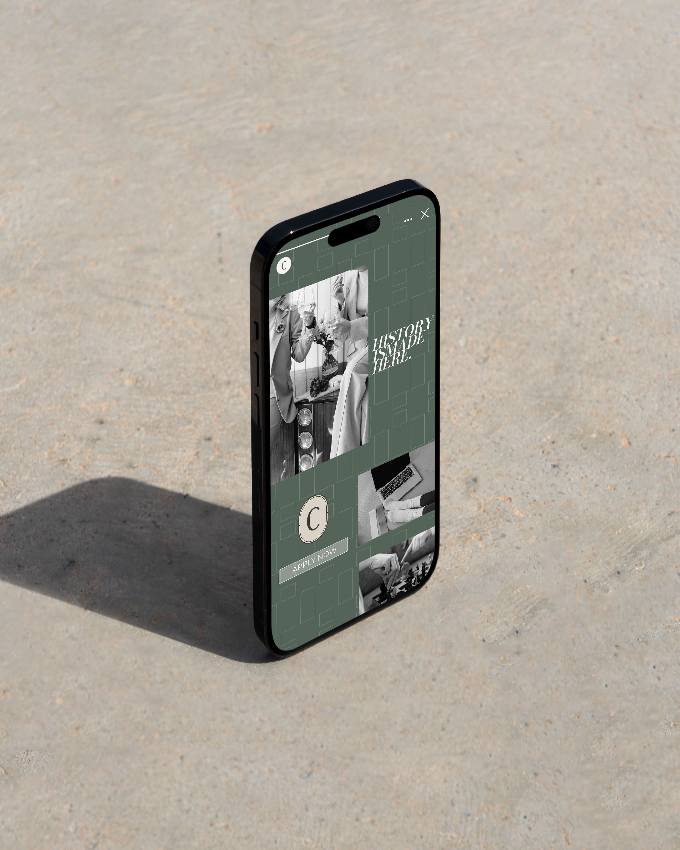 A smartphone stands upright on a concrete surface, displaying a muted green app interface with black-and-white photos and the text "HISTORY TRAIL.