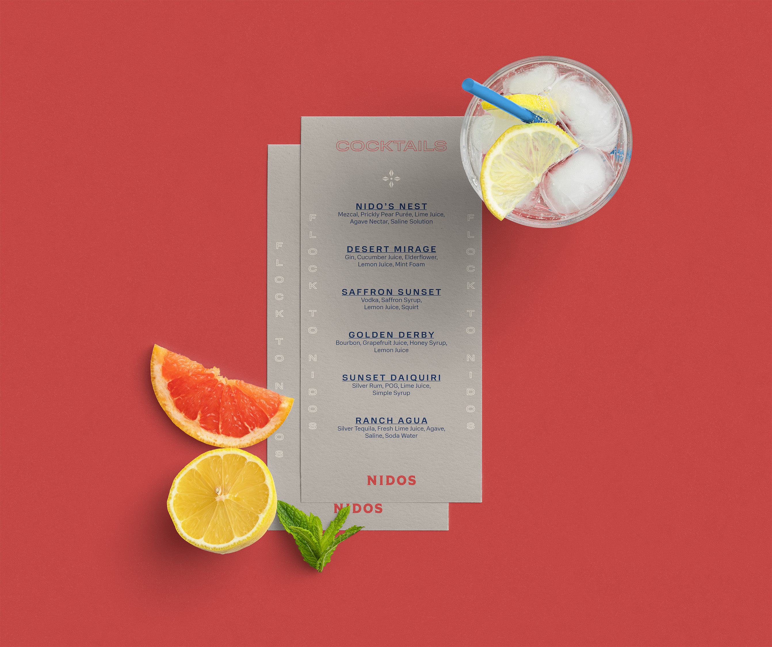 A cocktail menu on a red background with a glass of ice water, a lemon wedge, a grapefruit slice, a lemon half, and a mint sprig.