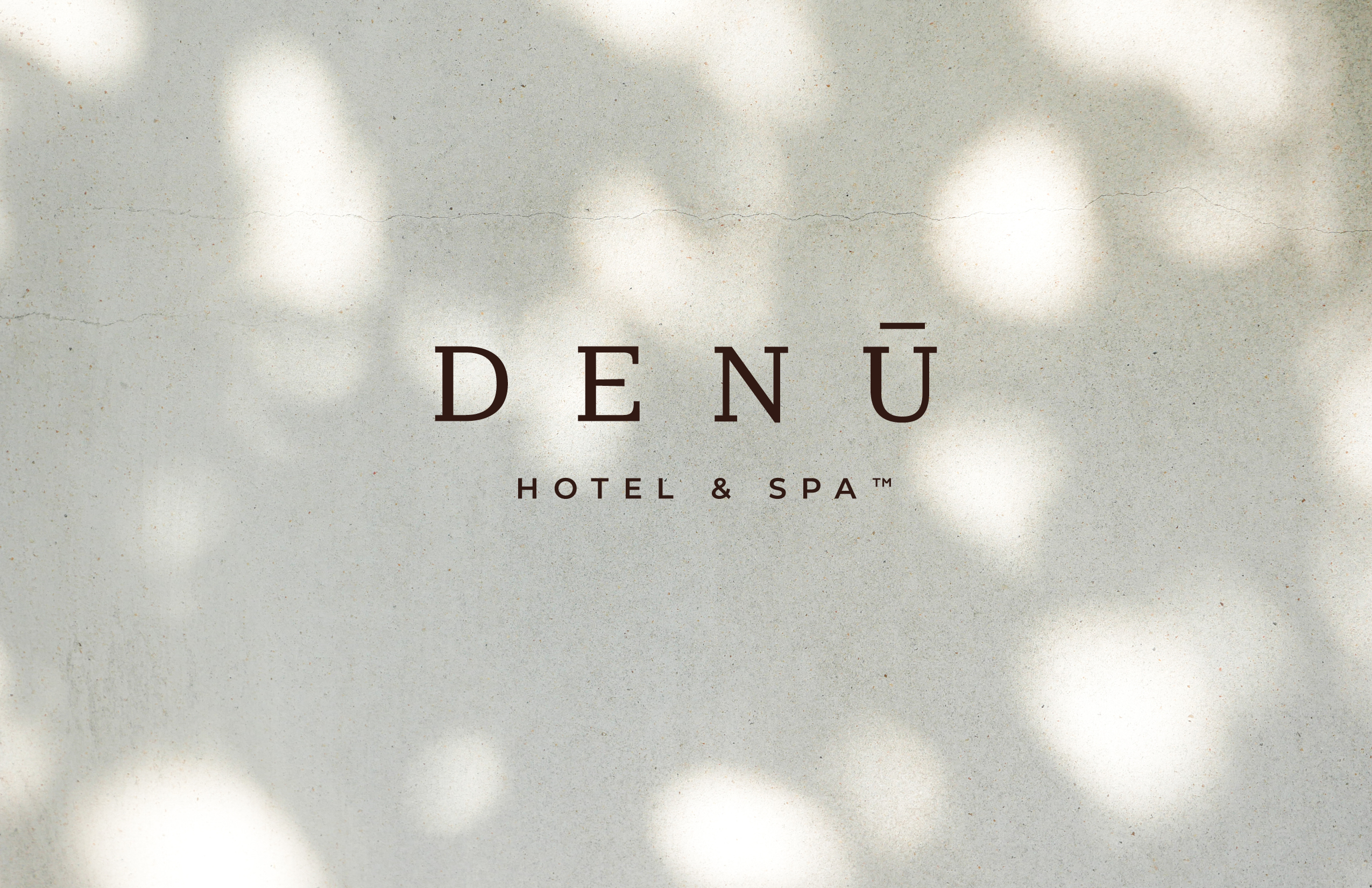 The words "DENŪ HOTEL & SPA™" appear in dark text on a light, textured background with soft, dappled sunlight.